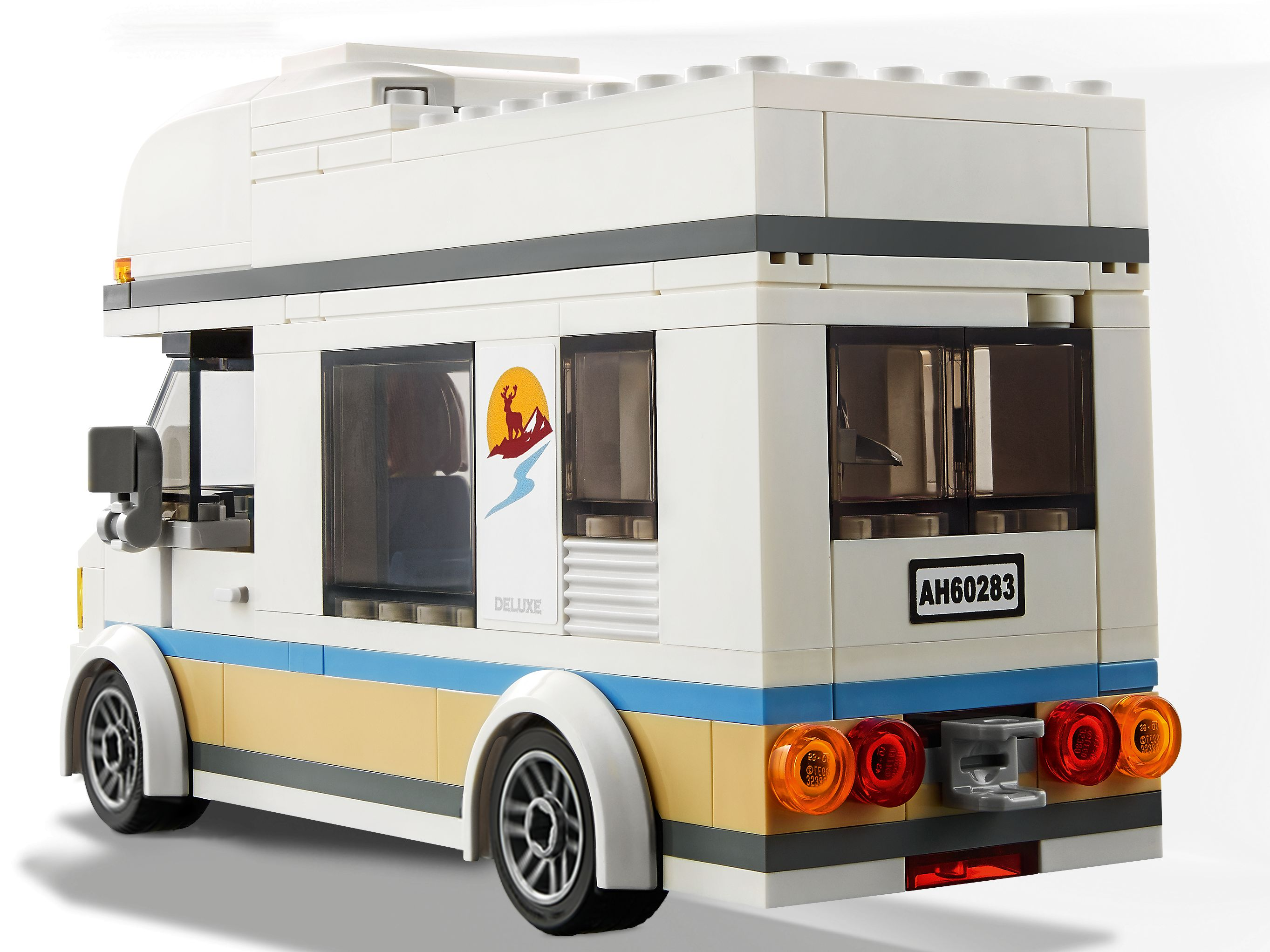 Un camper Lego bianco e beige. Ha una striscia blu, ruote nere e un adesivo con montagna e cervo.