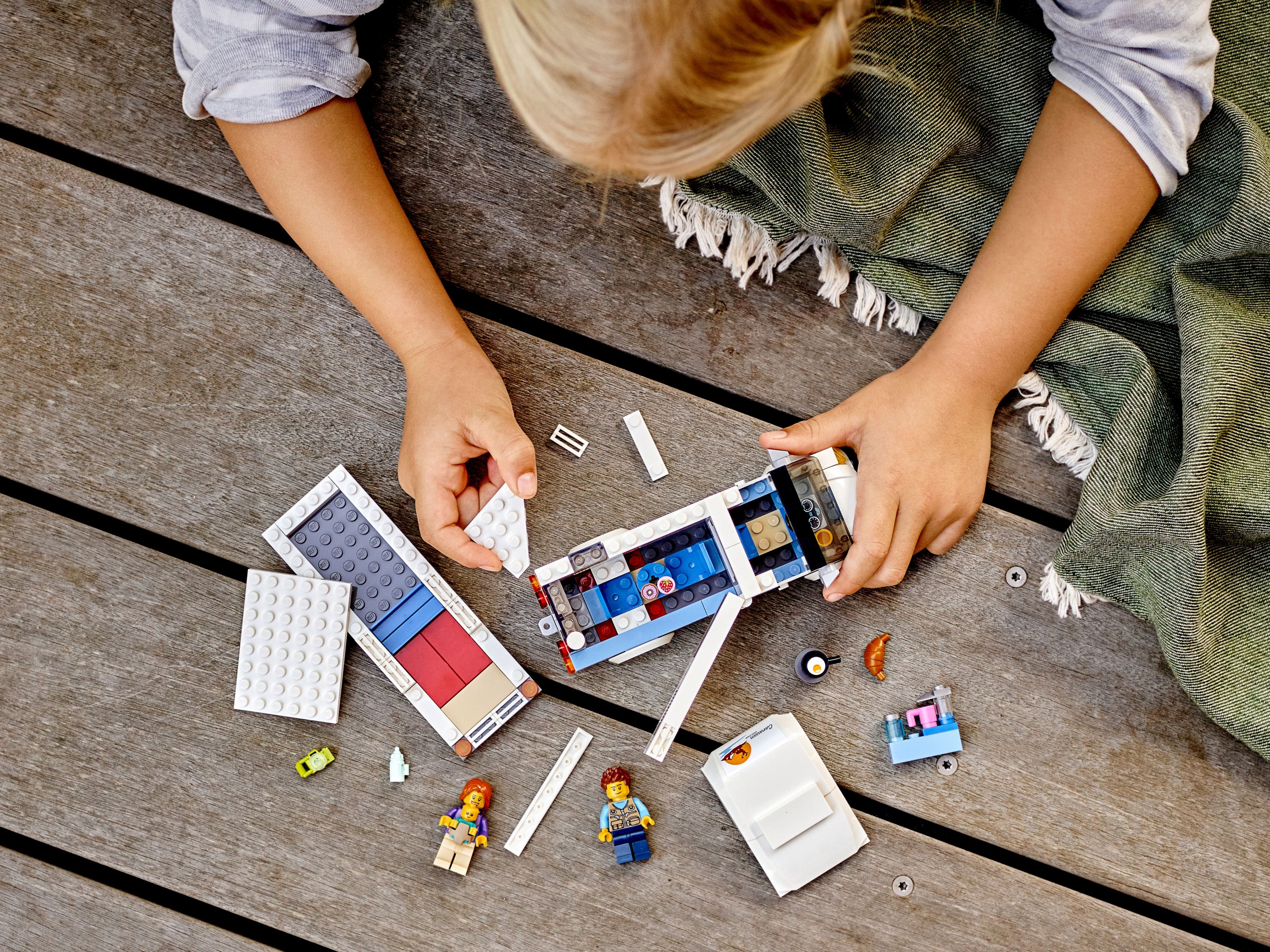 Un bambino gioca con i LEGO su una superficie di legno. Ci sono personaggi e pezzi LEGO e una coperta.