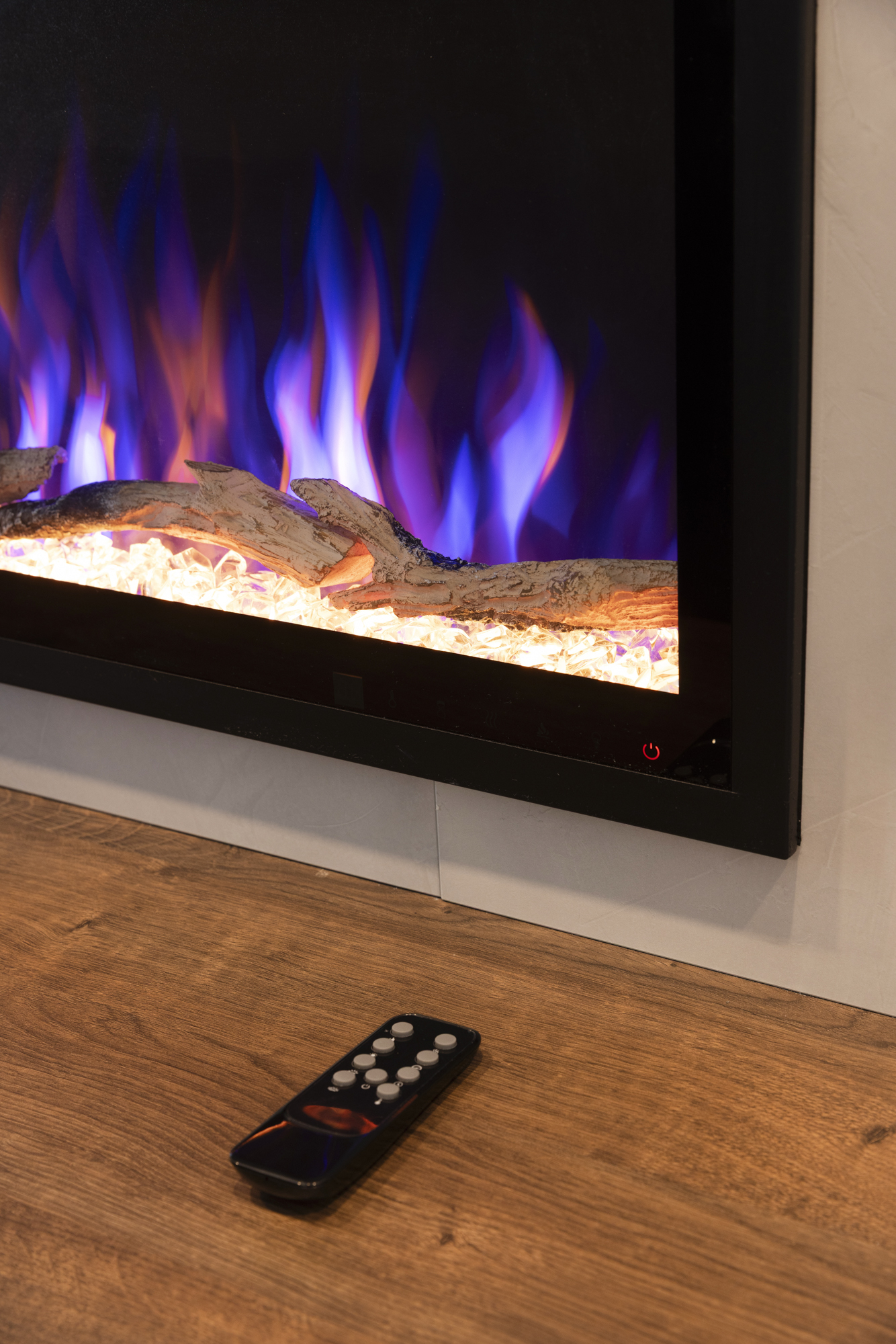 Chimenea eléctrica con llamas azules y naranjas. Un mando a distancia descansa sobre una superficie de madera.