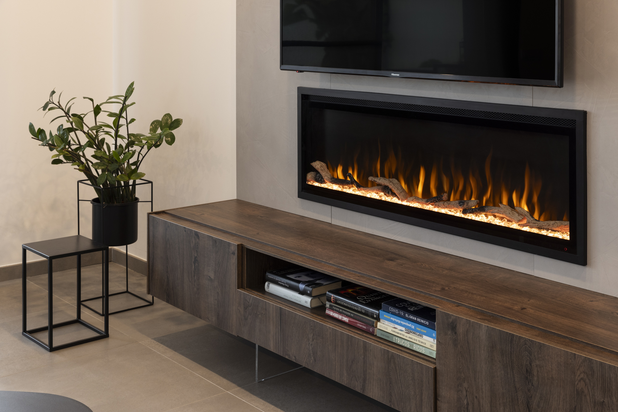 Salón moderno con chimenea, TV y mueble de madera con libros. Una planta está sobre una mesita auxiliar negra.