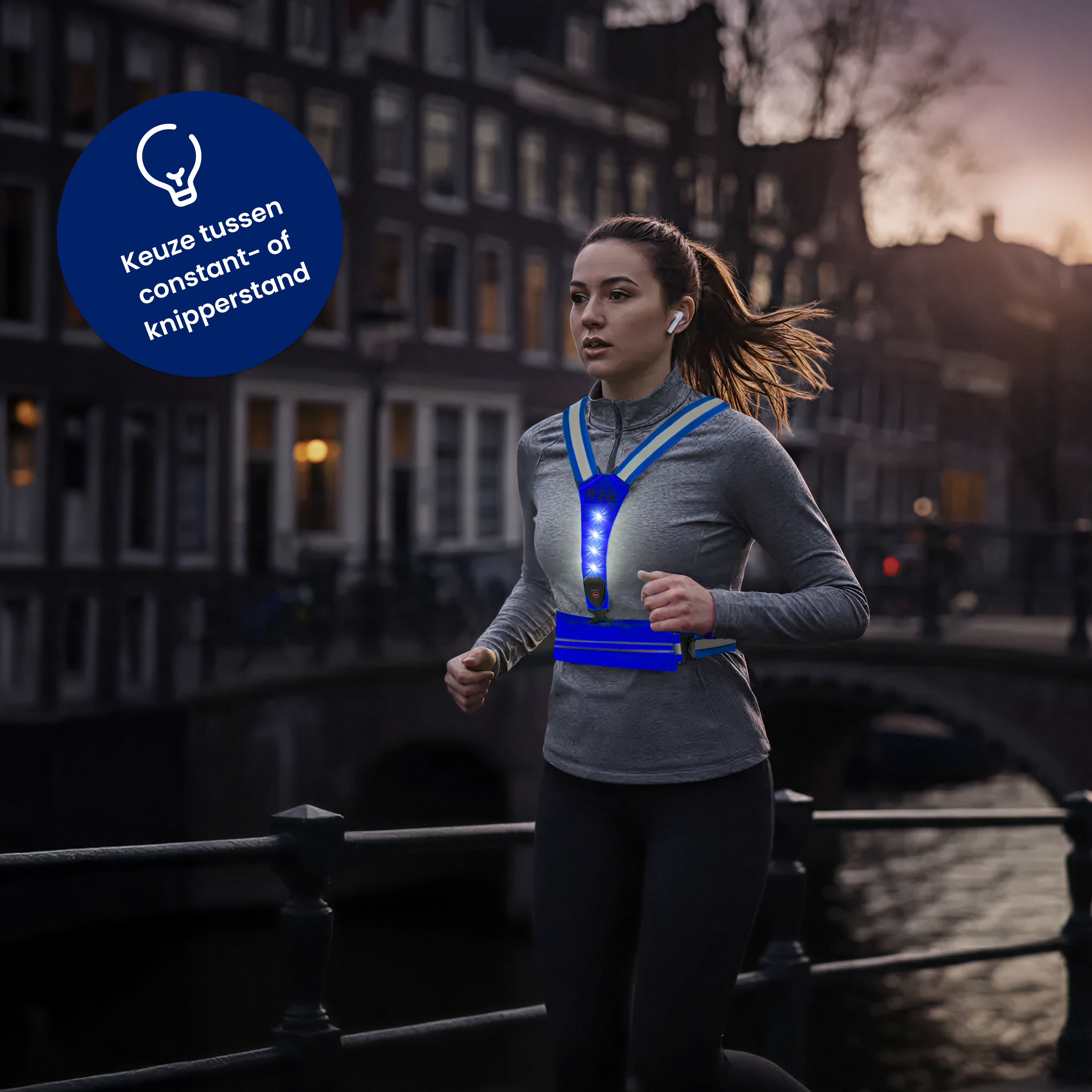 A woman runs wearing a blue, lighted vest in a city at dusk. Buildings and a bridge are in the background.