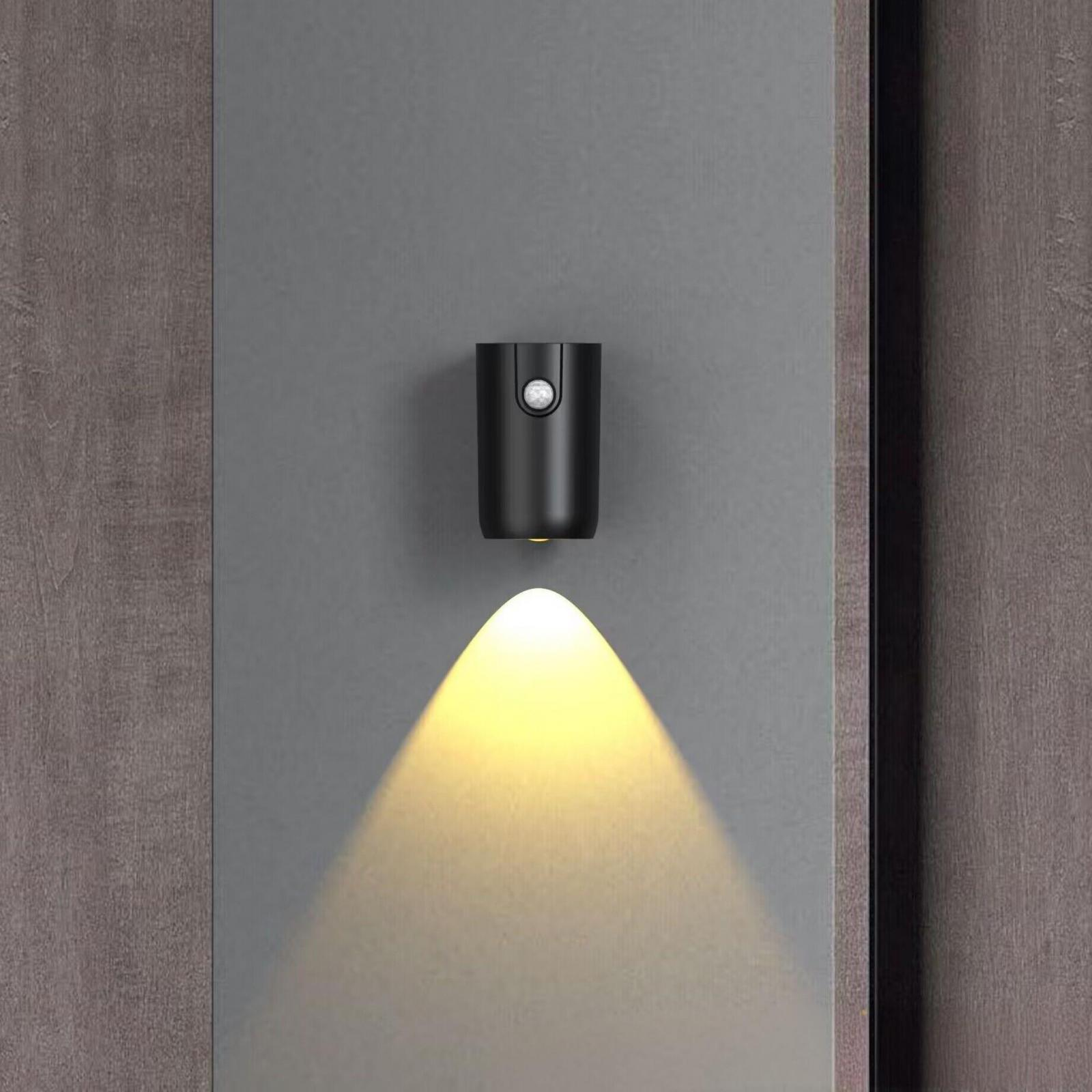 Eine schwarze, an der Wand montierte Leuchte mit einem nach unten gerichteten Strahl, an grauen Paneelen.