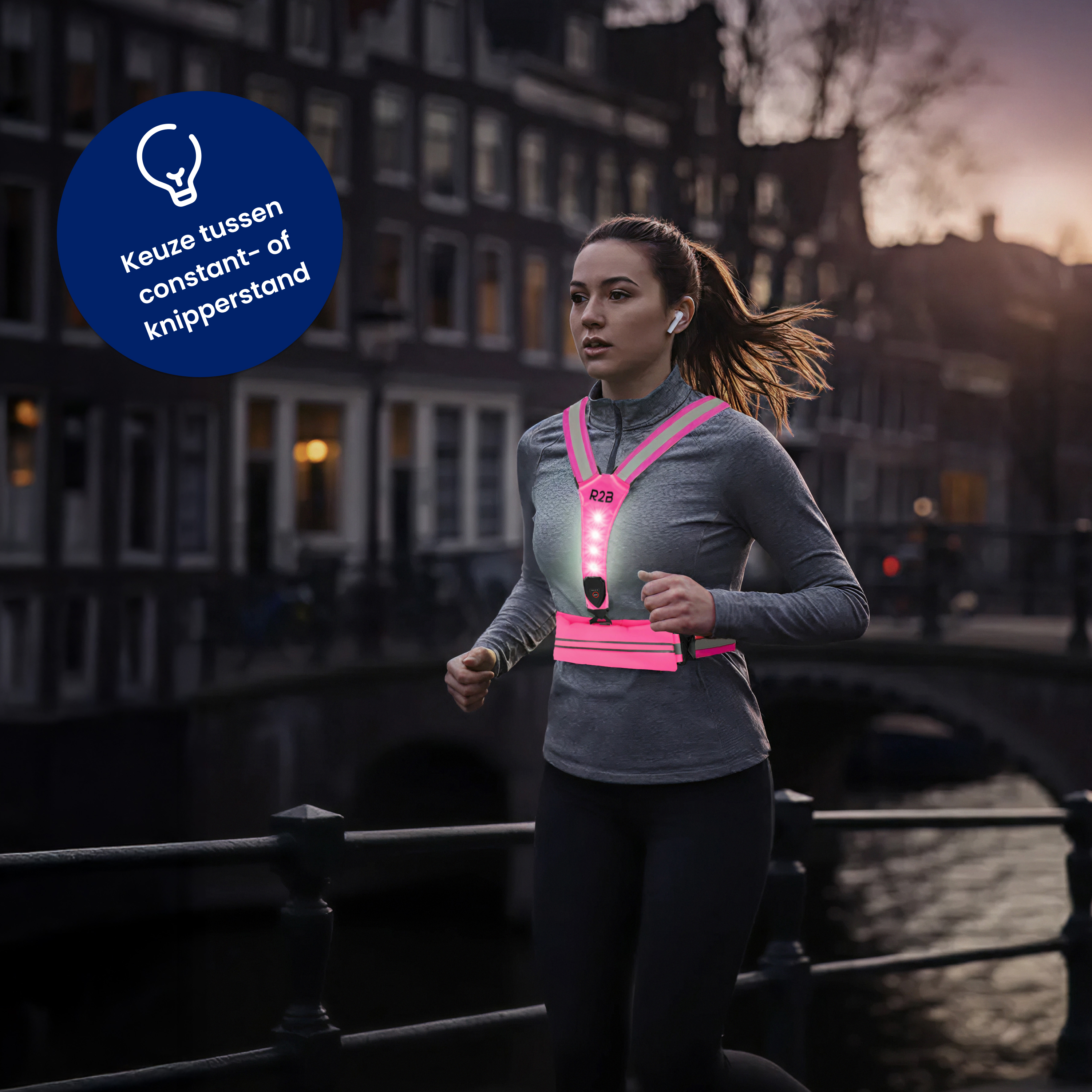 A woman runs wearing a pink safety vest with lights, in front of a bridge and buildings at dusk.