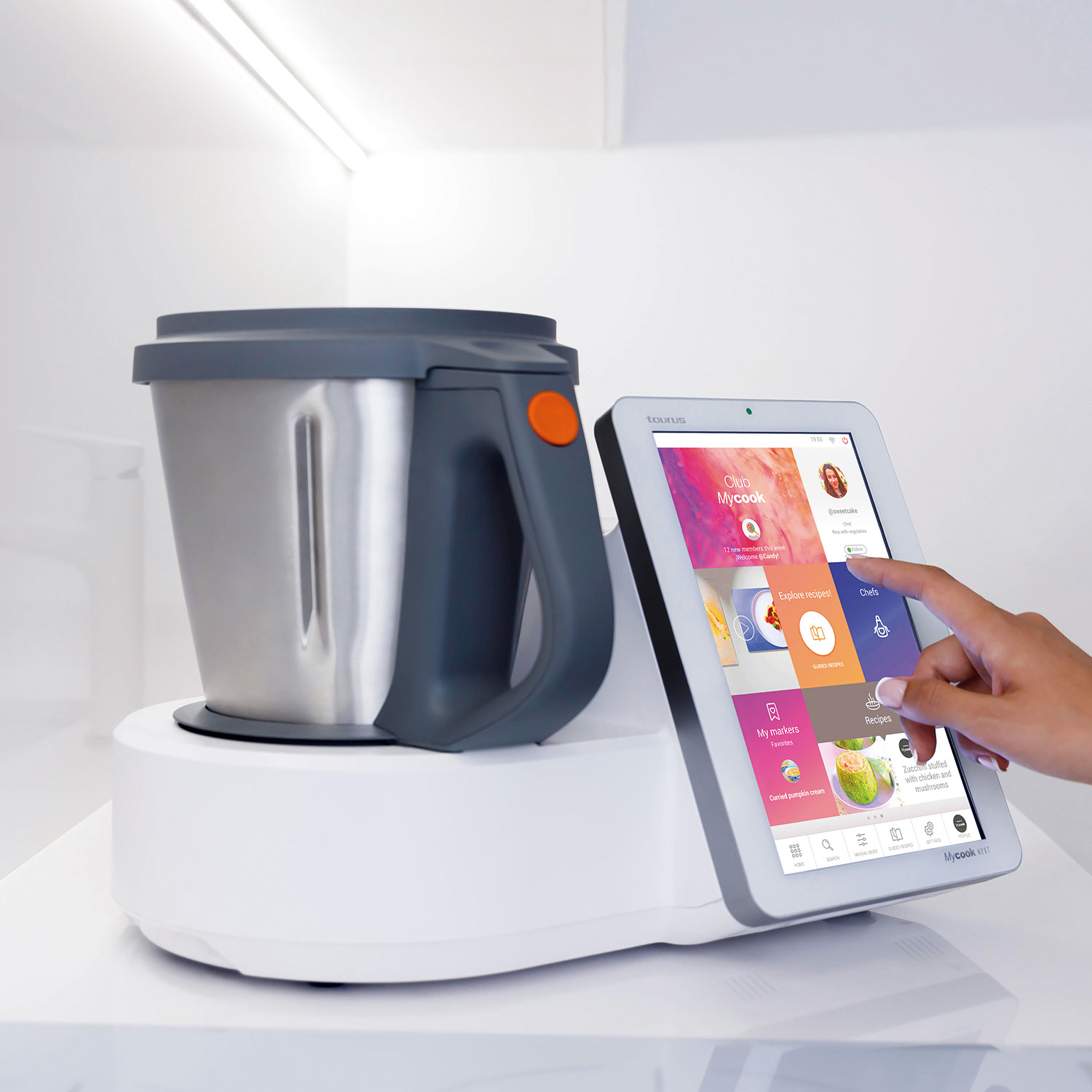 Un procesador de alimentos Taurus Mycook con una tableta que muestra una aplicación de recetas. Una mano toca la pantalla.