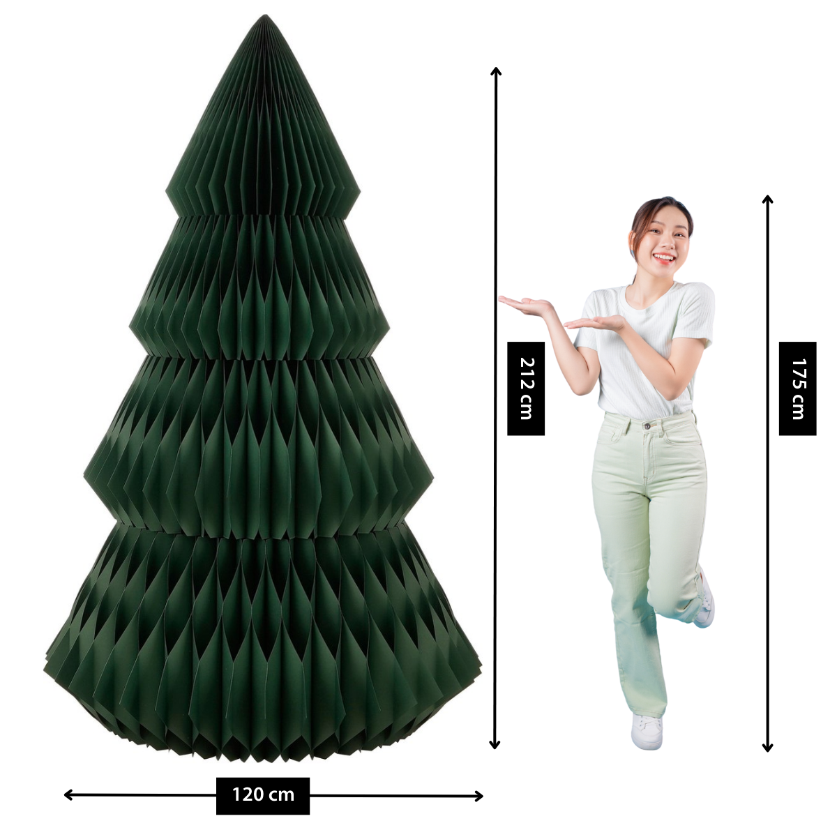 Une femme se tient à côté d'un sapin de Noël en papier, en montrant. L'arbre est vert foncé et mesure 120 cm de large, 212 cm de haut. La femme mesure 175 cm.