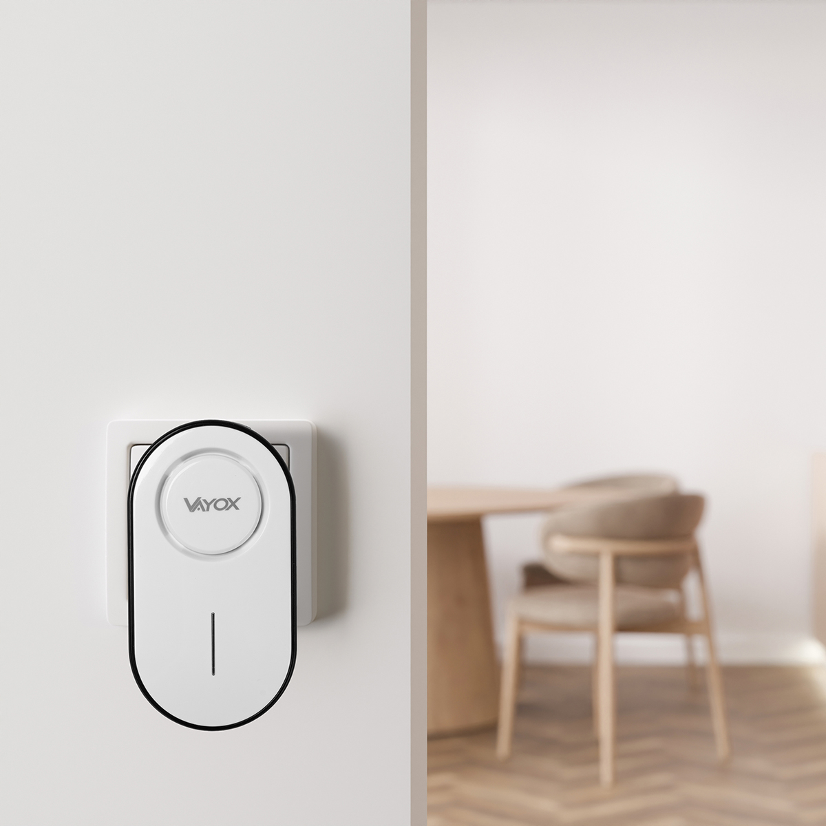 Biały dzwonek do drzwi z czarną obwódką i logo Vayox jest zamontowany na białej ścianie. W tle widać rozmyty jadalnię.