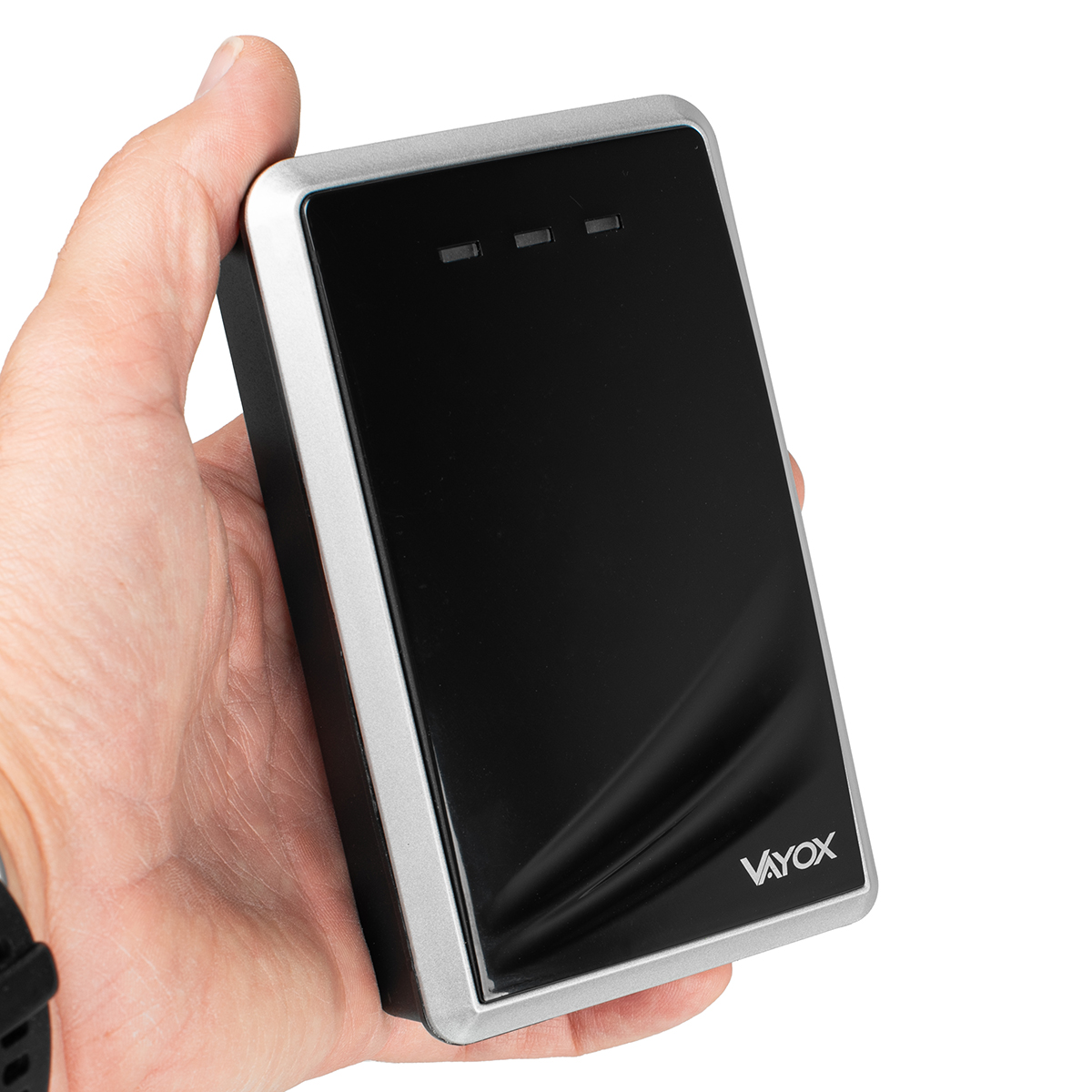 Ręka trzyma czarno-srebrne urządzenie Voyox. Urządzenie ma trzy małe światełka i logo Voyox.