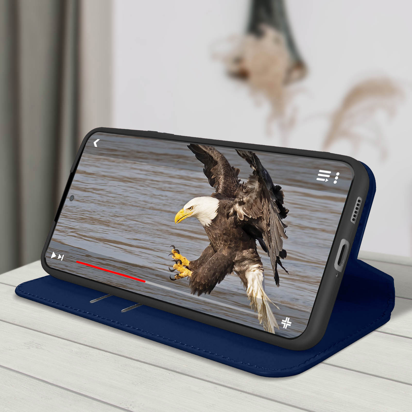 Un téléphone affiche un aigle en vol au-dessus de l'eau. Il est dans un étui bleu sur une surface en bois blanc.