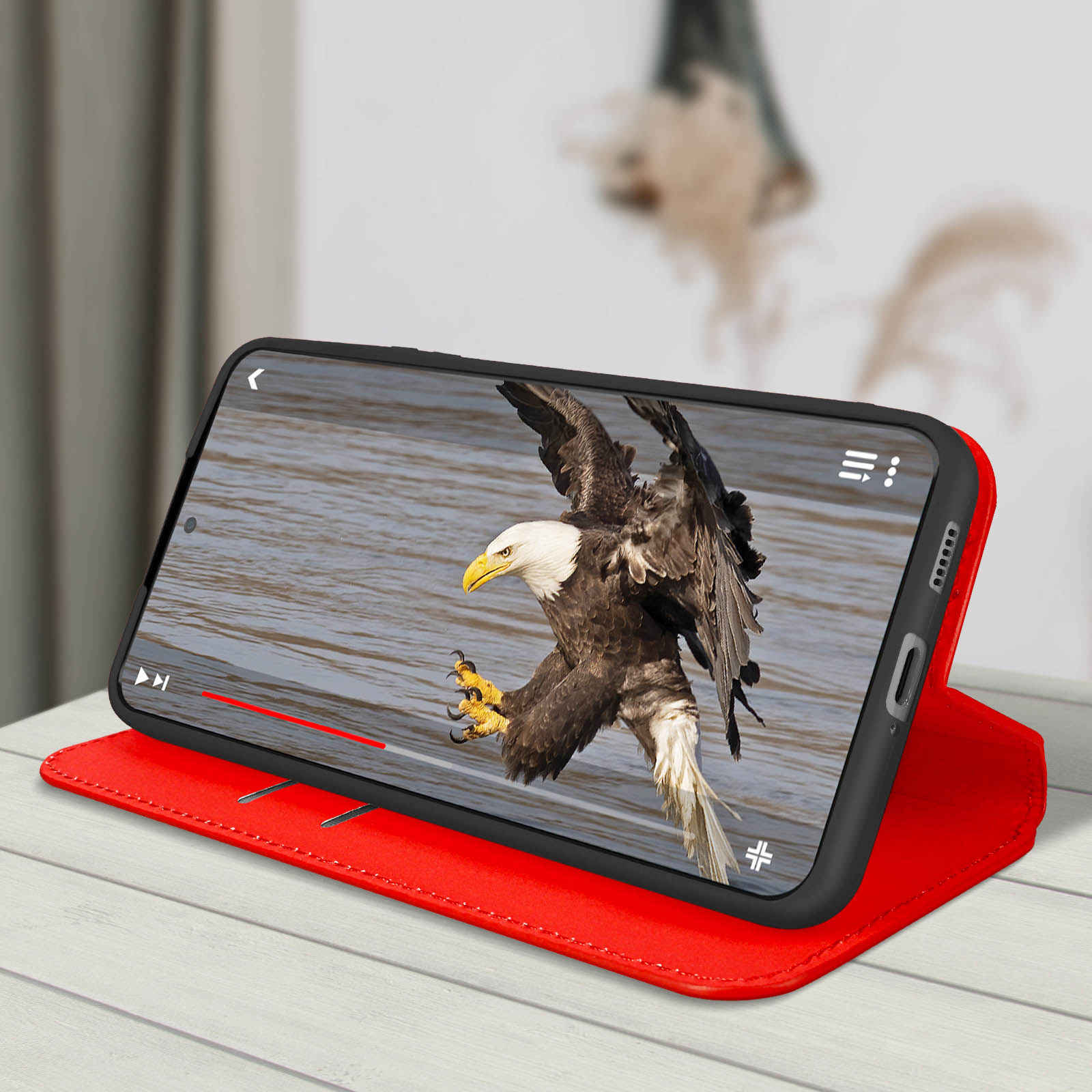 Téléphone affichant un aigle atterrissant. Le téléphone est dans un étui rouge, sur une surface en bois blanc. Arrière-plan flou.