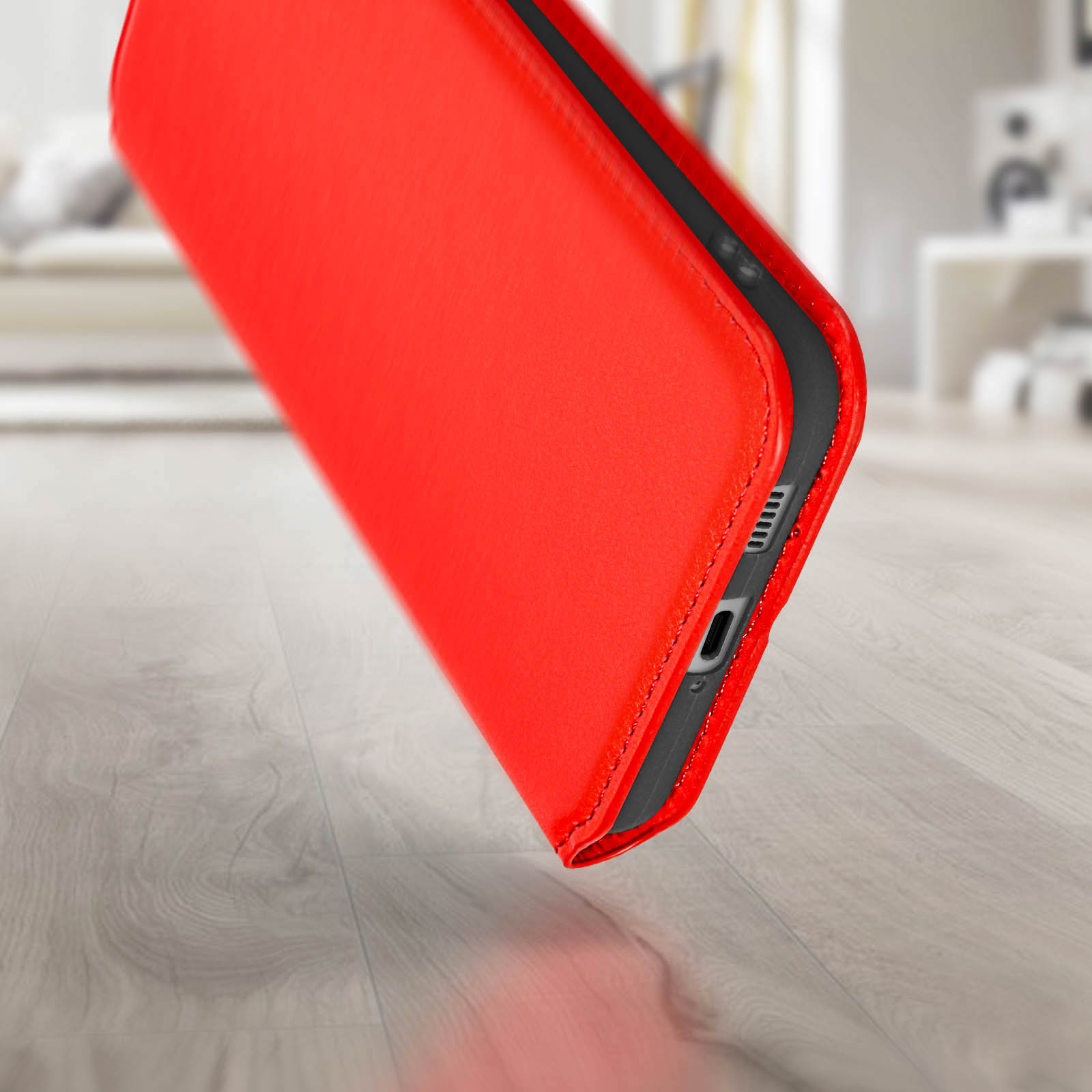 Un étui de téléphone rouge est posé sur un sol en bois. L'étui est incliné, montrant le côté avec le port de charge.