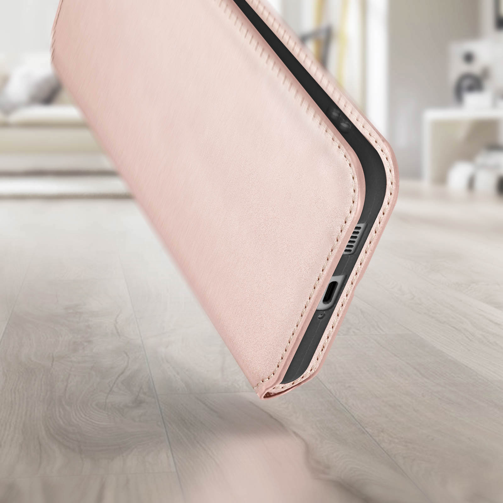 Un étui de téléphone or rose sur une surface en bois. L'étui a une surface texturée avec des coutures.
