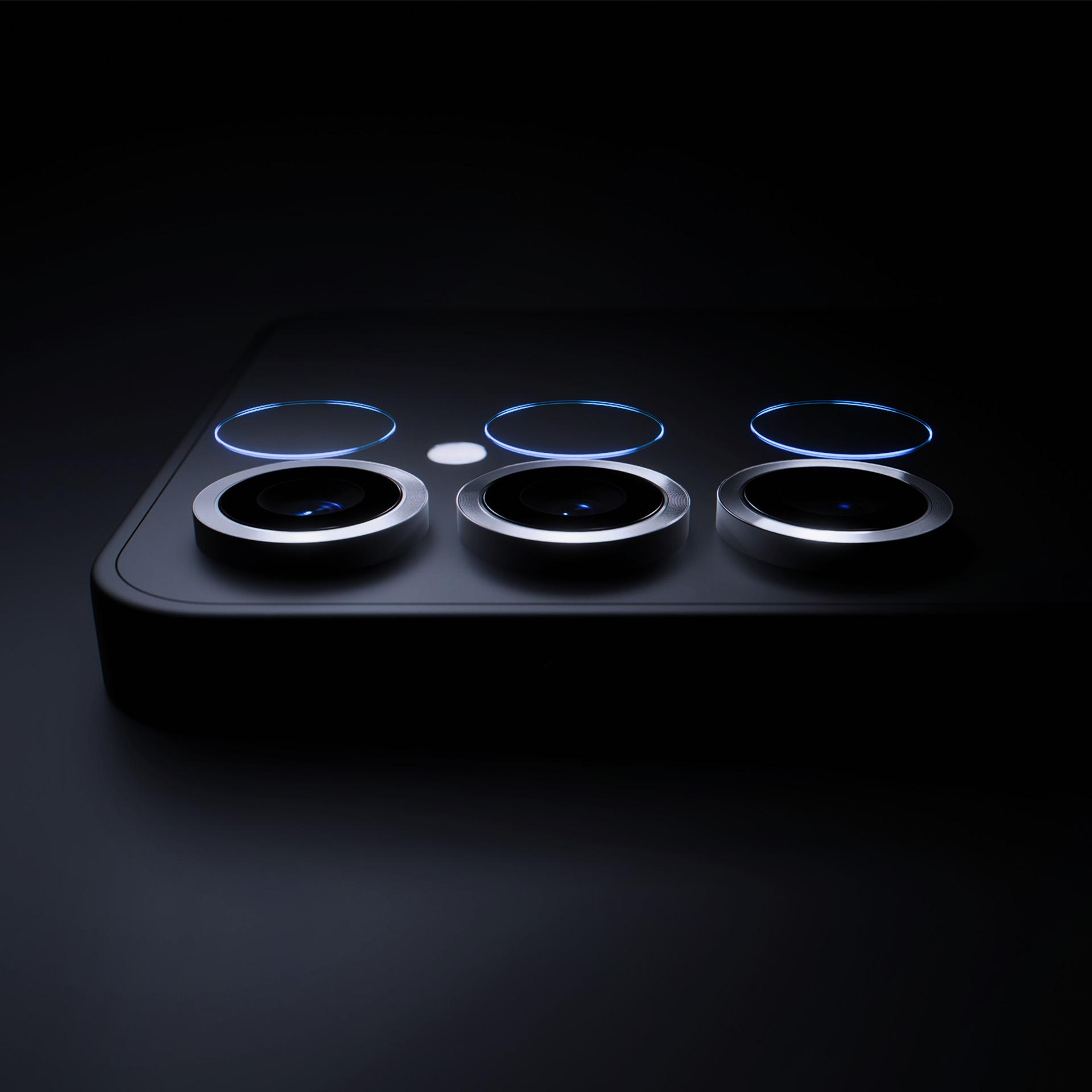 Zbliżenie modułu aparatu w smartfonie z trzema obiektywami i podświetlanymi pierścieniami, ciemne tło.