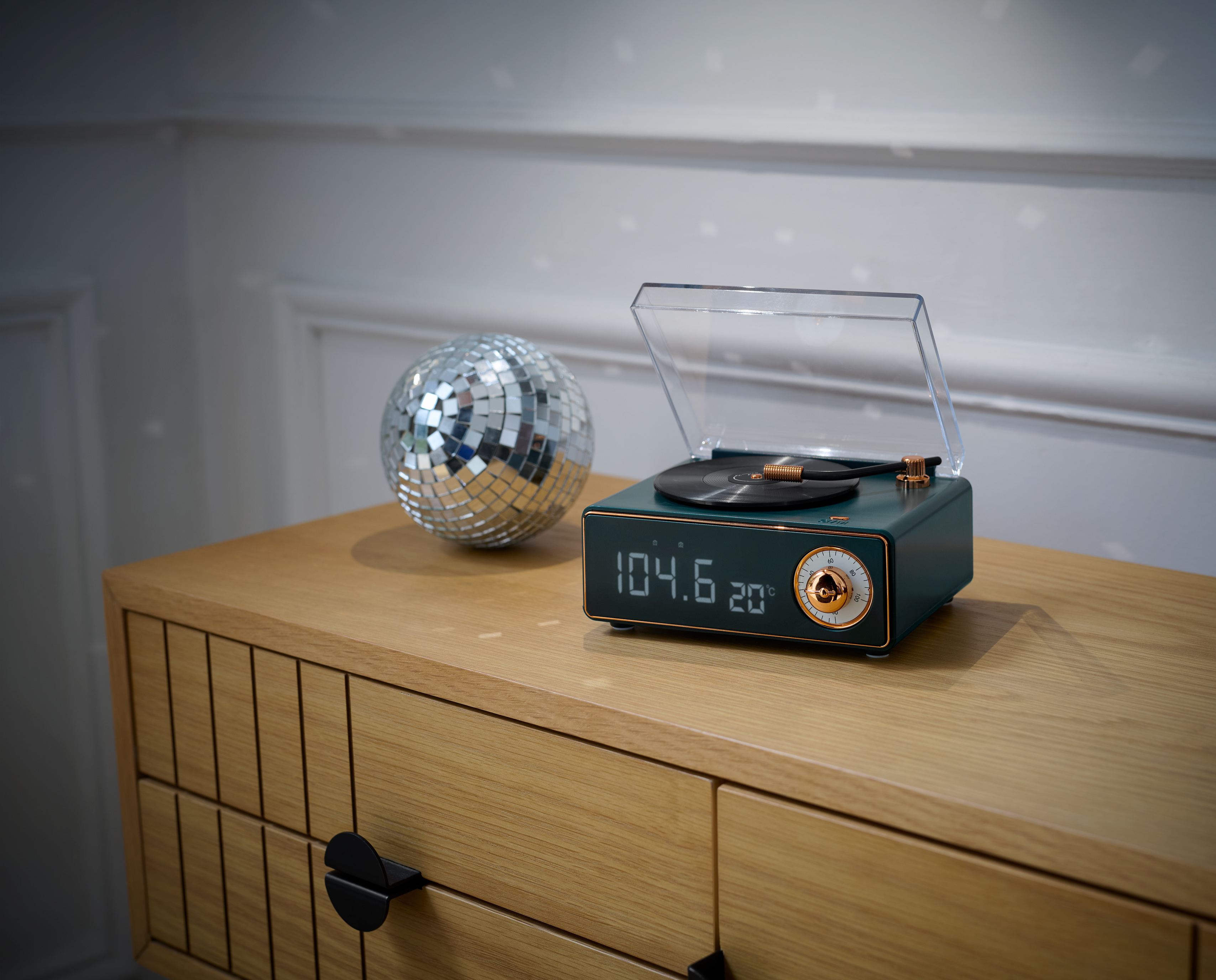Une platine avec affichage numérique et une boule disco sur une armoire en bois, contre un mur blanc.