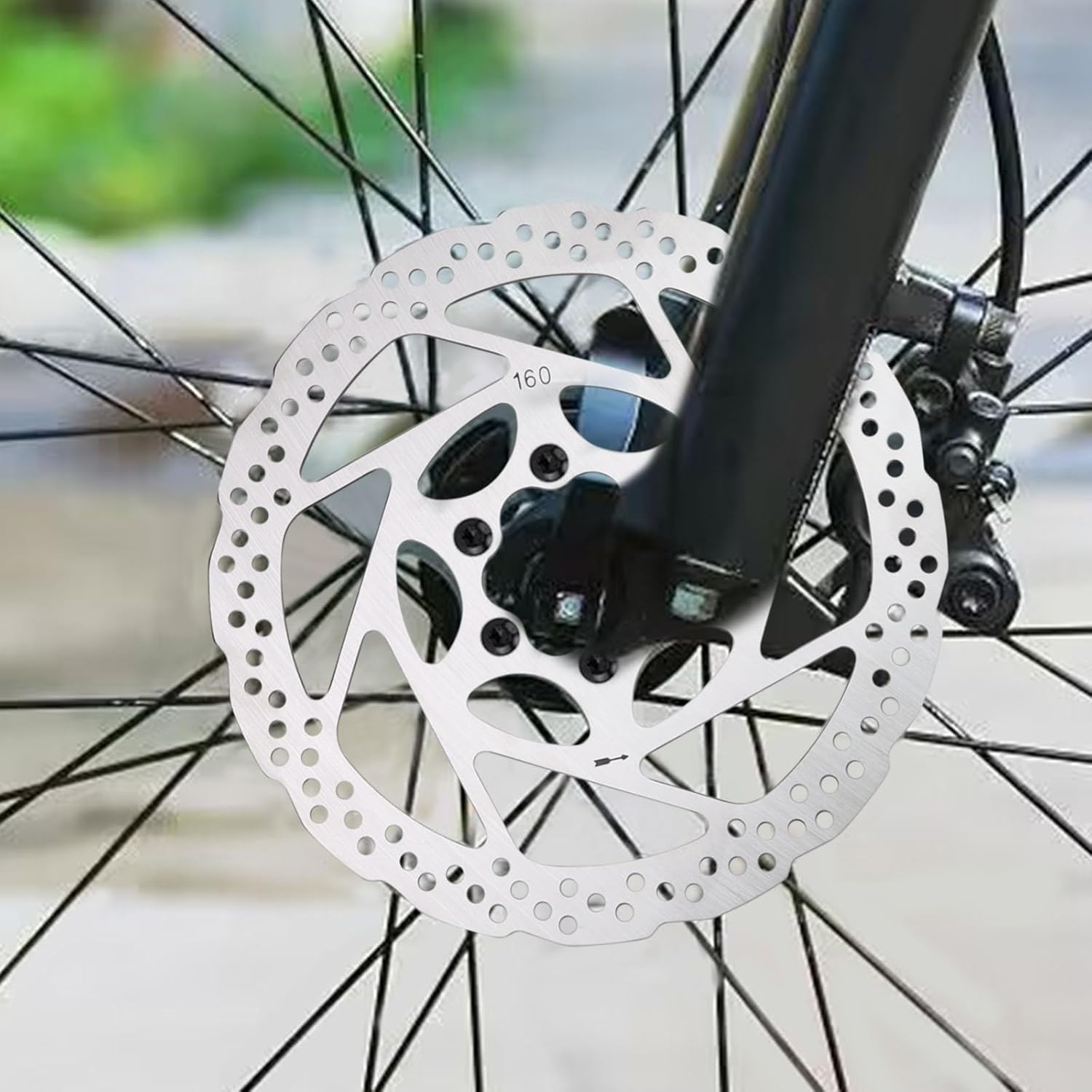 Nahaufnahme einer Fahrrad-Scheibenbremse. Silberne Scheibe mit Löchern, schwarze Gabel und Speichen. Verschwommener Hintergrund.