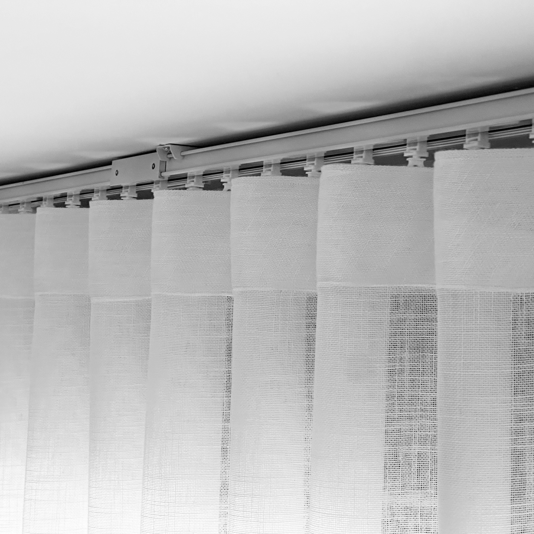 Nahaufnahme von weißen Vorhängen, die an einer Schiene an der Decke hängen. Die Vorhänge sind leicht gerafft.