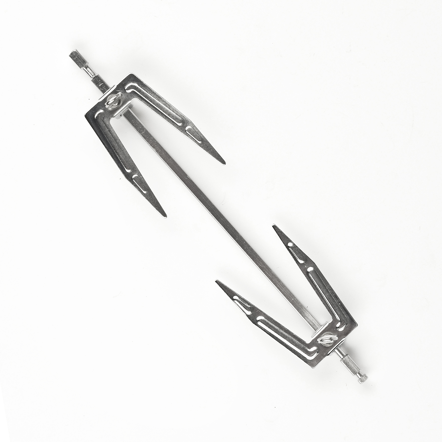 Metalowy widelec do rożna leży na białej powierzchni. Ma dwa widelce na każdym końcu i centralny pręt.