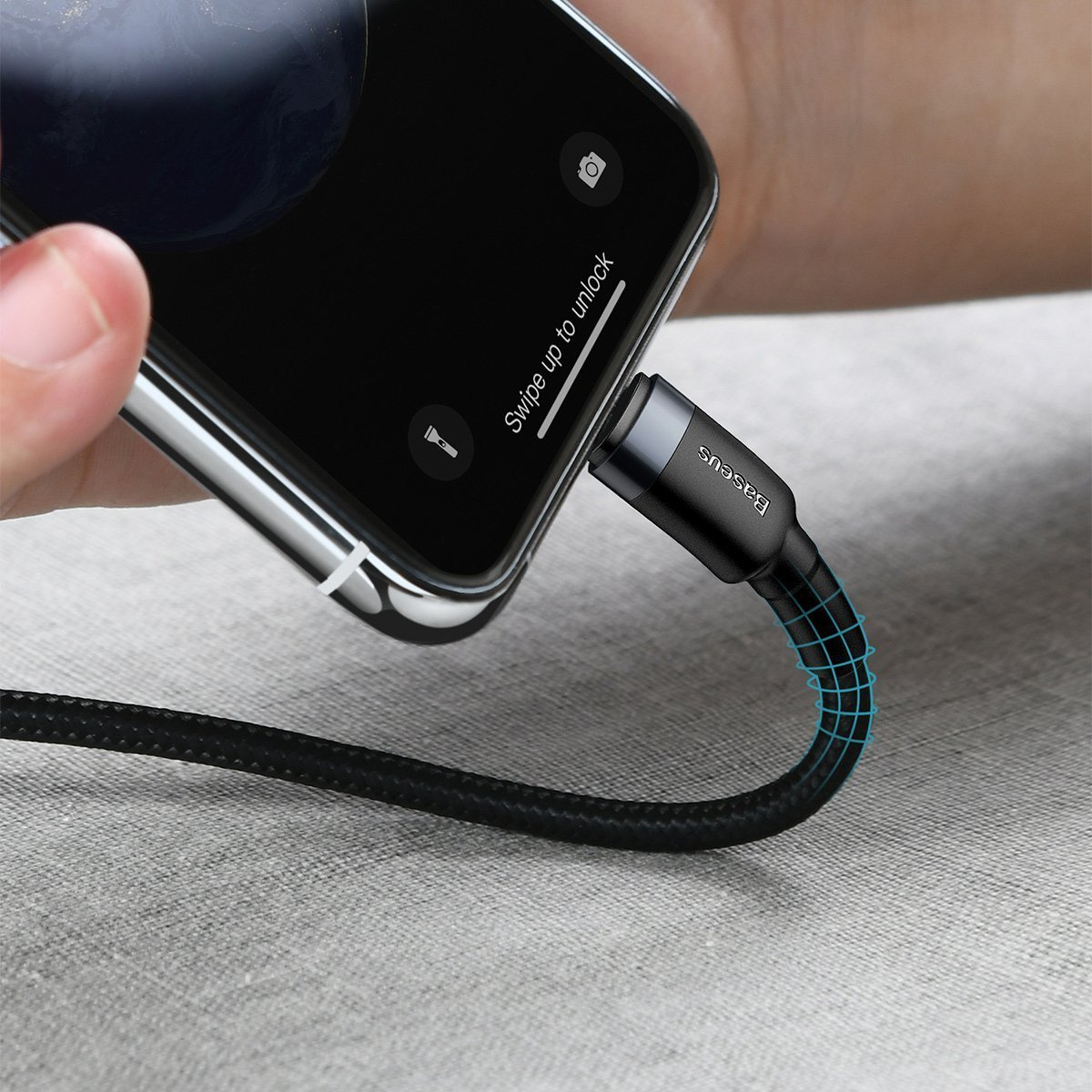 Telefon jest ładowany czarnym kablem. Ręka trzyma telefon. Na ekranie widnieje napis 'Przesuń w górę, aby odblokować'.