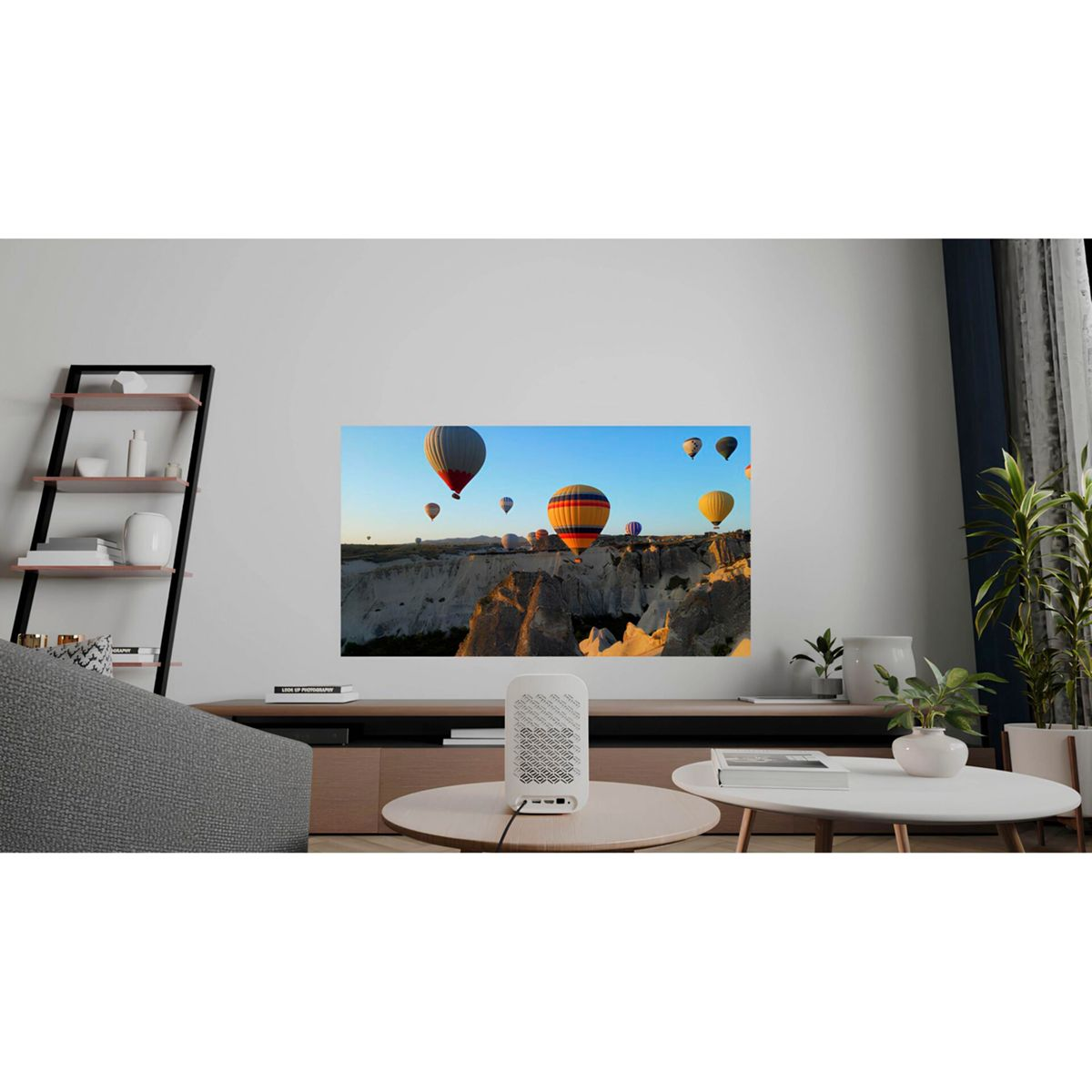 Wohnzimmer mit TV, der Heißluftballons über einem Canyon zeigt. Weißer Tisch mit Gerät, Regalen und Pflanze.