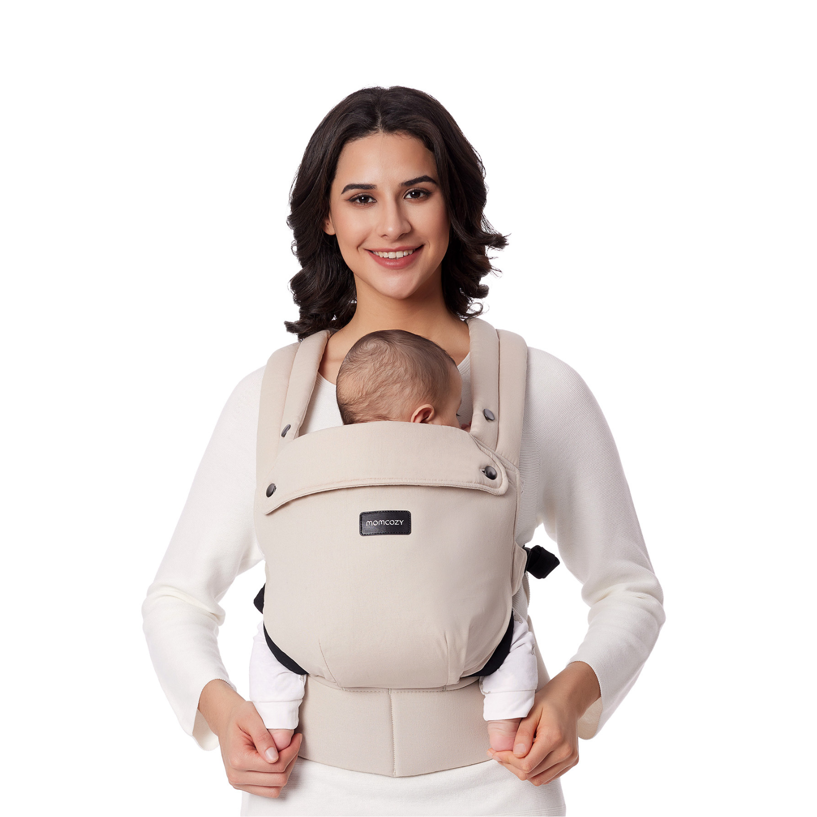 A woman smiles, holding a baby in a beige carrier. The baby's head is visible. White background.