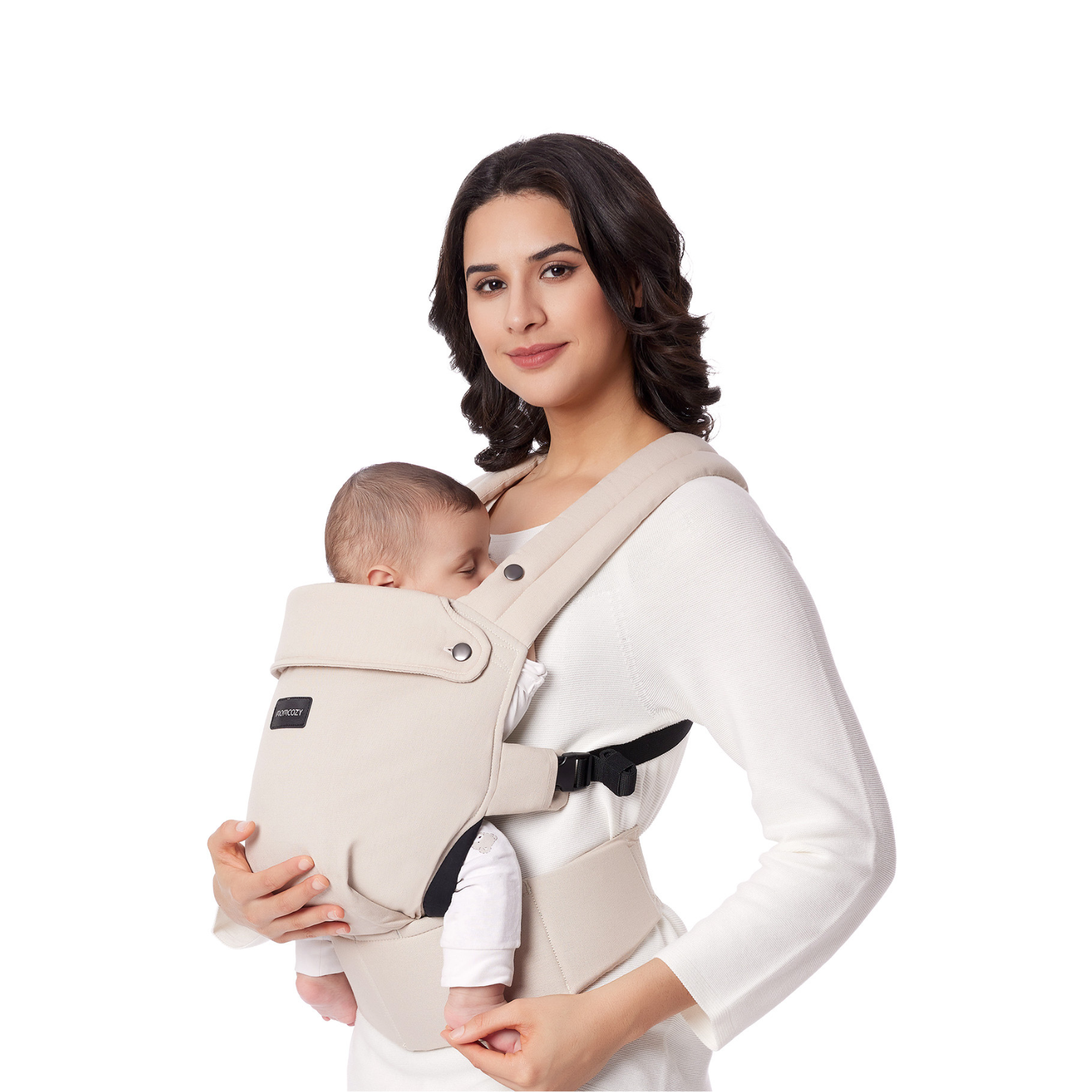 A woman holds a baby in a beige carrier. The woman wears a white sweater. The baby is sleeping.