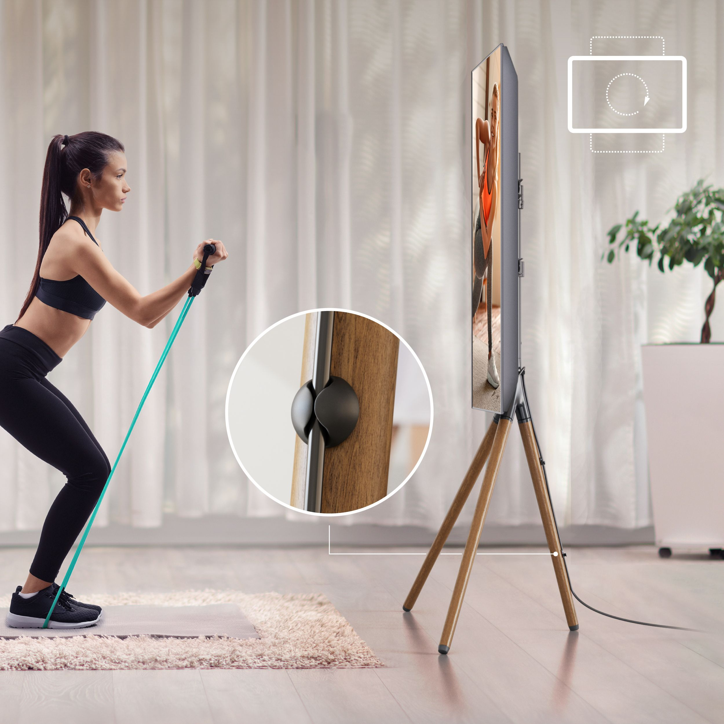 Kobieta ćwiczy z taśmą oporową w pobliżu telewizora na drewnianym stojaku. Zasłony i roślina w tle.