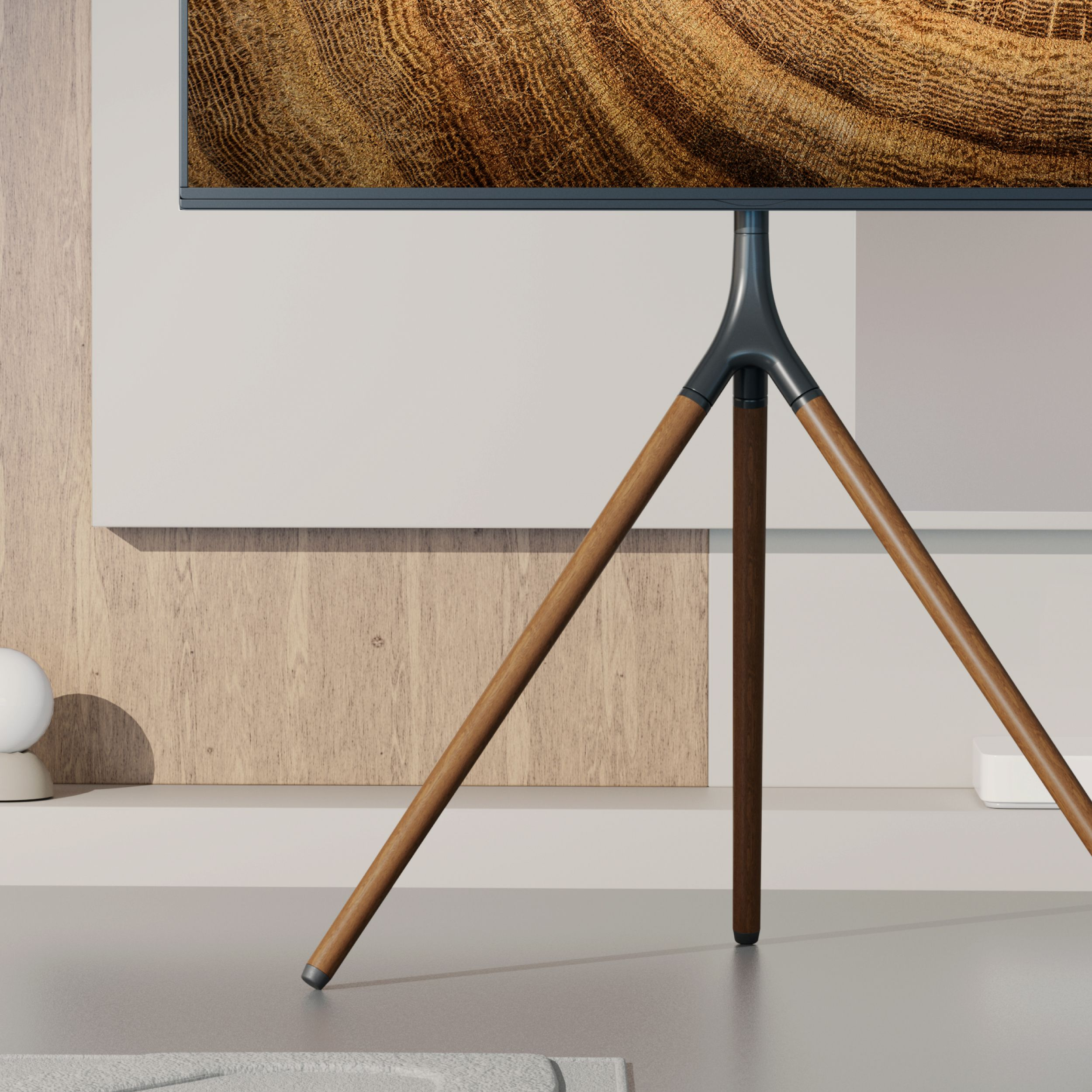 Telewizor na statywie, drewniane nogi. Tło, ściana z drewnianym panelem i jasna półka.