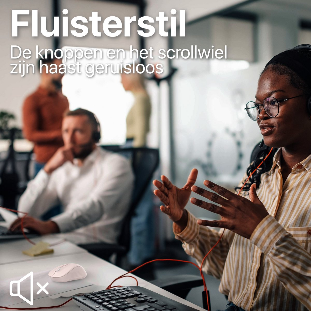 Een vrouw met bril en headset spreekt. Een muis en toetsenbord liggen vooraan. Twee mannen en een vrouw zijn op de achtergrond.