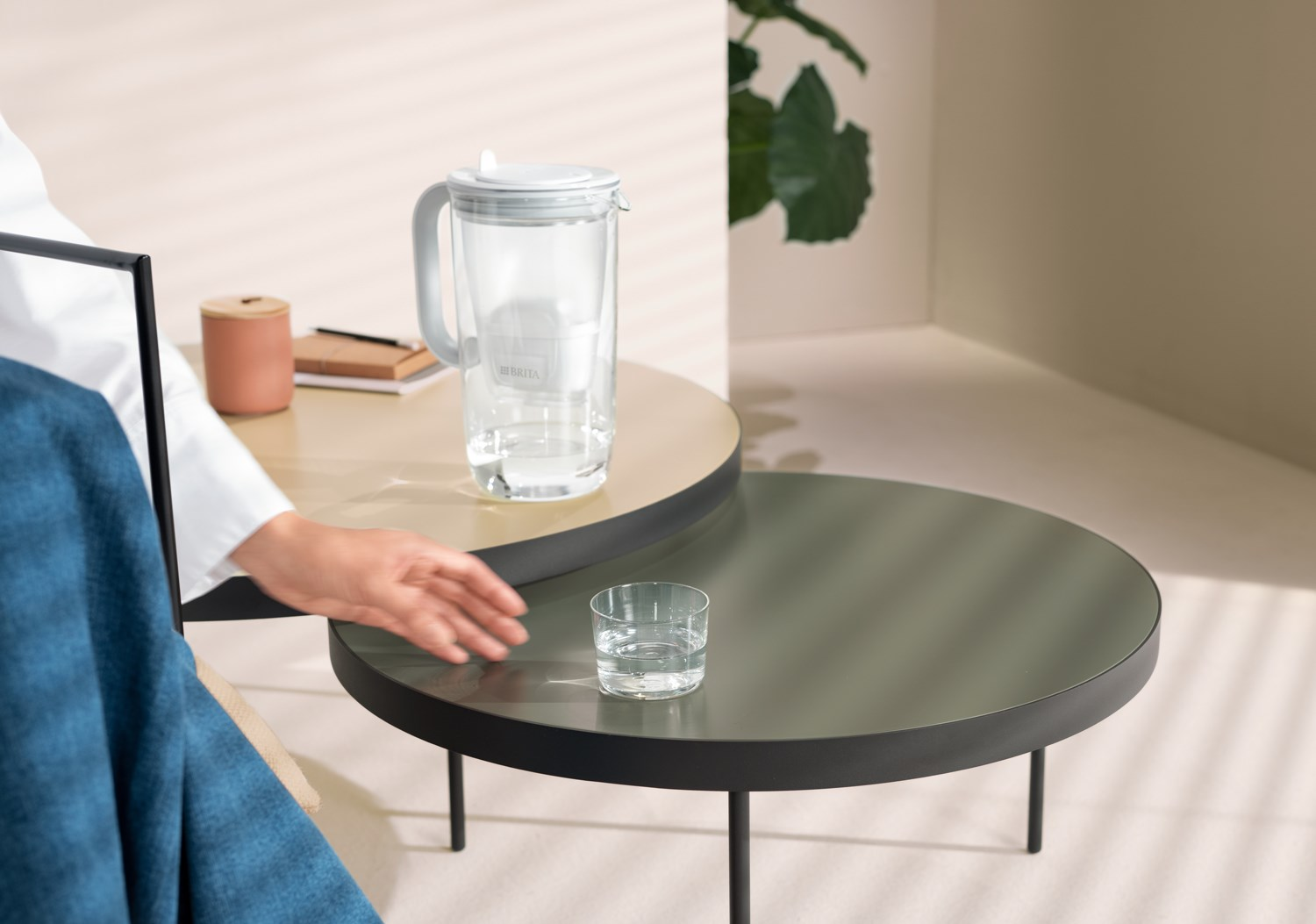 Ręka sięga po szklankę wody na stole. Widoczny jest również dzbanek z wodą i inne przedmioty.