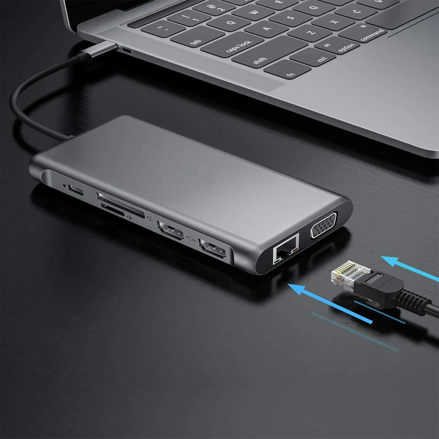 Ein grauer USB-Hub ist mit einem Laptop verbunden. Ein Ethernet-Kabel ist mit dem Hub verbunden. Alles auf einem schwarzen Schreibtisch.