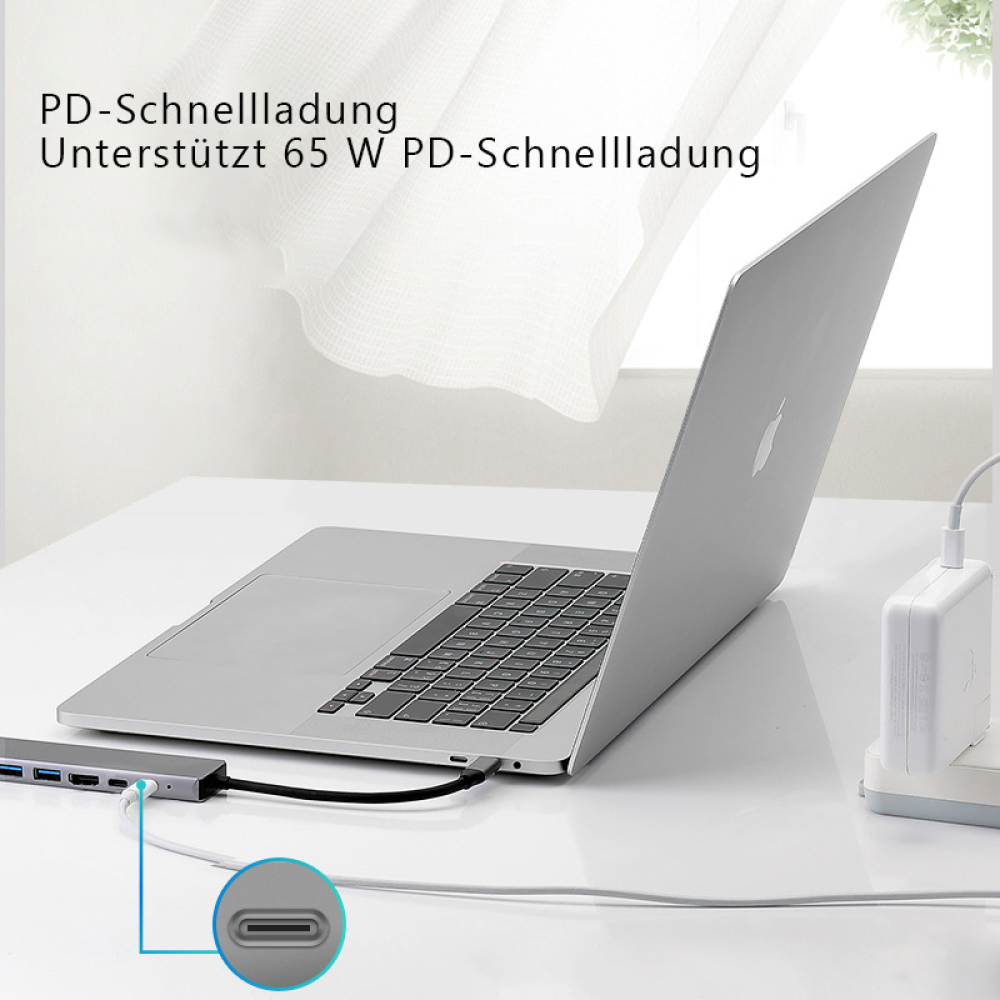 Ein silberner Laptop ist auf einem weißen Schreibtisch geöffnet. Ein Ladegerät und ein Hub sind angeschlossen. Text auf Deutsch.