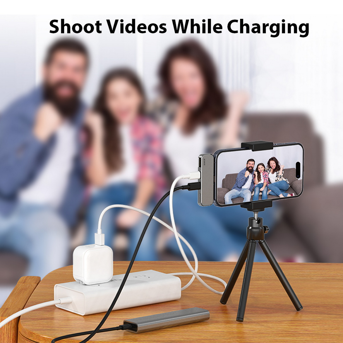 Ein Telefon auf einem Stativ nimmt eine Familie auf, die über verschiedene Kabel mit einer Steckdosenleiste und einem Adapter geladen wird. Personen sind im Hintergrund unscharf.