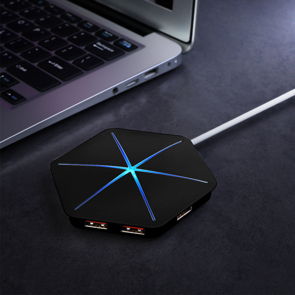 Ein schwarzer USB-Hub mit blauem Licht ist mit einem Laptop verbunden. Der Hub hat USB-Anschlüsse und ein weißes Kabel. Der Hintergrund ist dunkel.