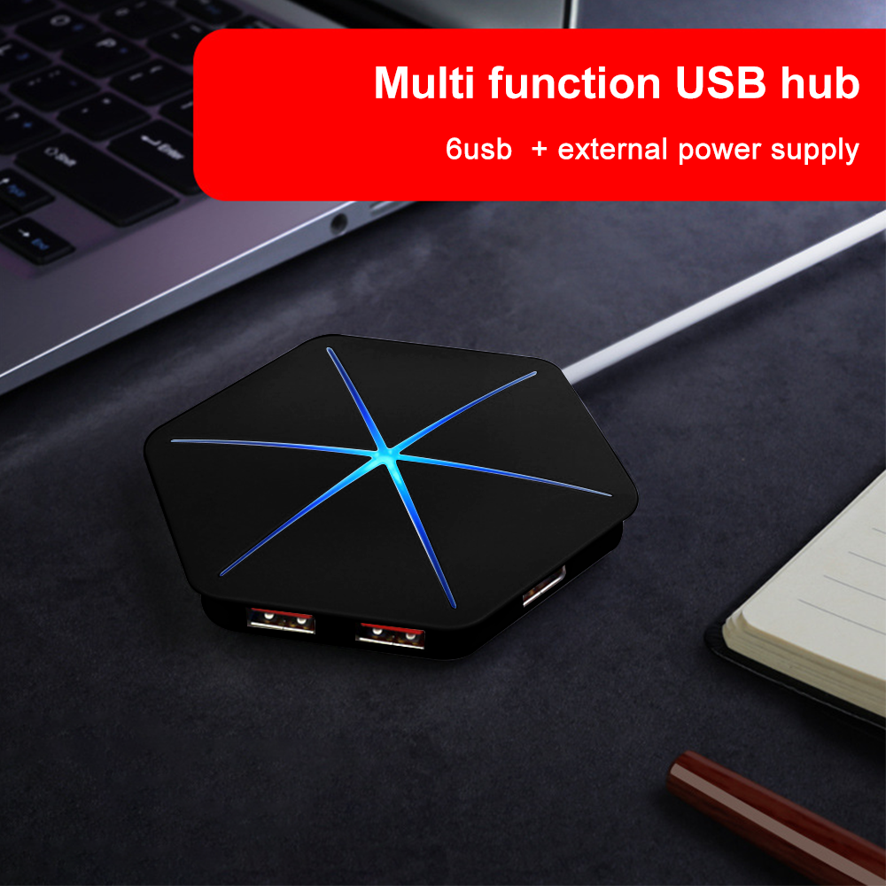 Ein schwarzer USB-Hub mit blauen Lichtern, verbunden mit einem Laptop. Ein Notizbuch und ein Stift liegen auf der dunklen Oberfläche.