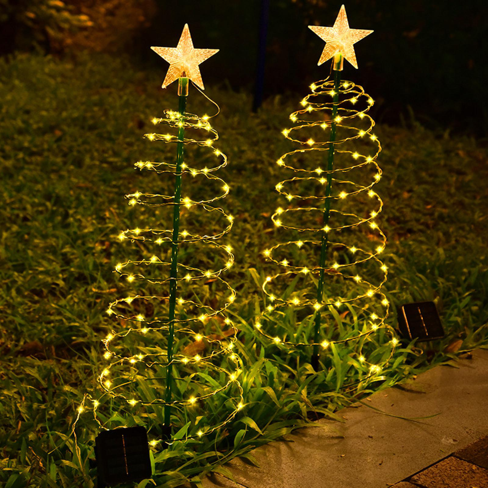 Zwei dekorative, spiralförmige Weihnachtsbäume mit Sternaufsätzen, beleuchtet mit warmweißen Lichtern, im Gras.