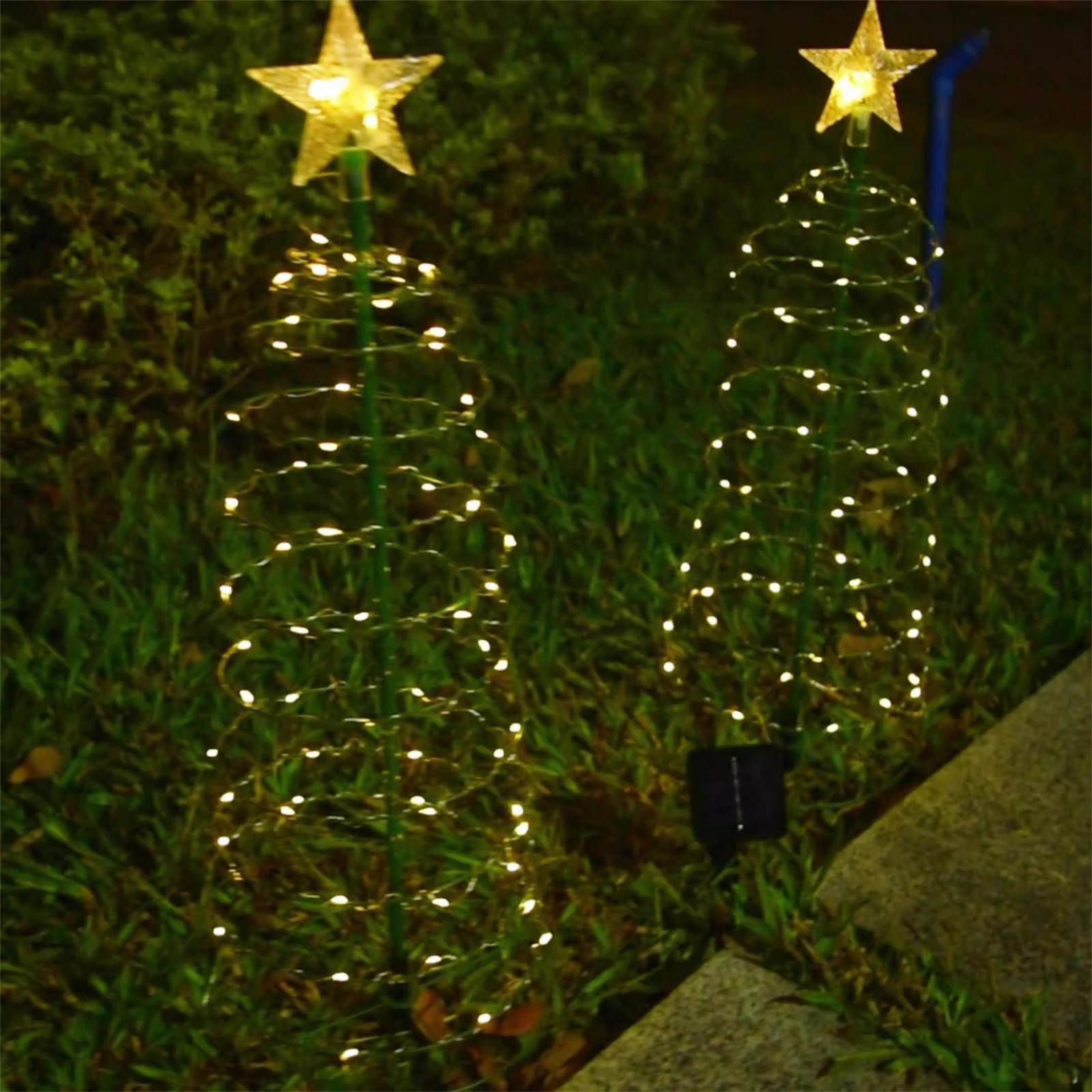 Zwei dekorative, spiralförmige Weihnachtsbäume mit Sternaufsätzen, beleuchtet mit kleinen Lichtern, auf Gras platziert.