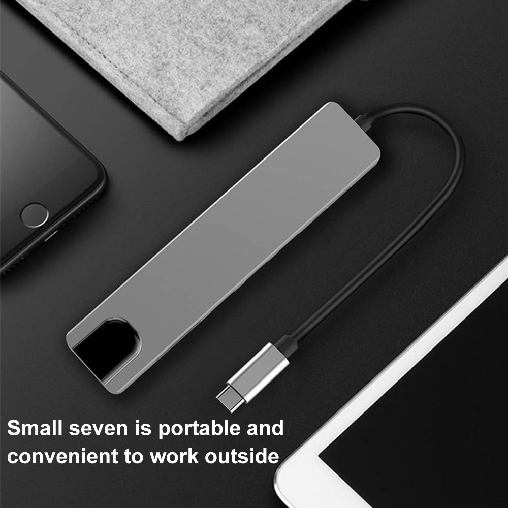 Ein silberner USB-C-Hub mit schwarzem Kabel. Ein Smartphone und ein Tablet sind in der Nähe. Ein graues Filzpad liegt auf der schwarzen Oberfläche.