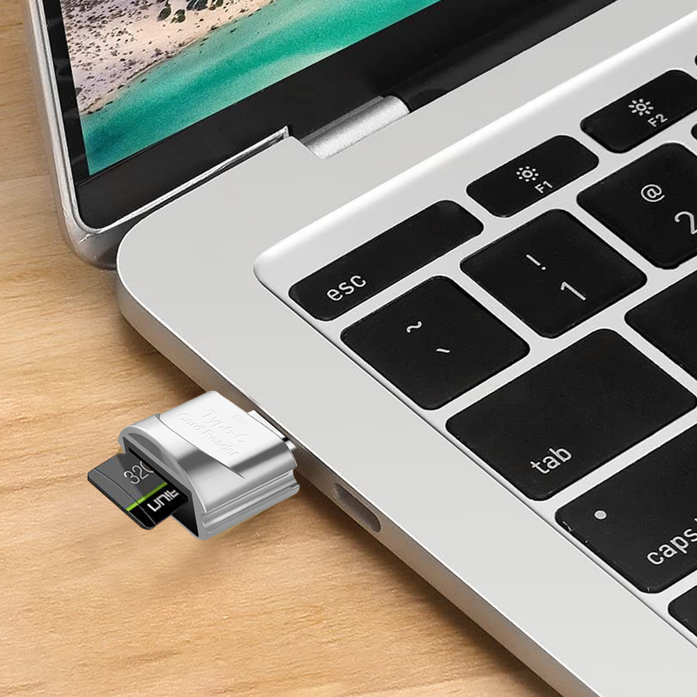 Ein silbernes Kartenlesegerät mit einer schwarzen SD-Karte ist an einen Laptop angeschlossen. Die Tastatur ist schwarz mit weißer Beschriftung.
