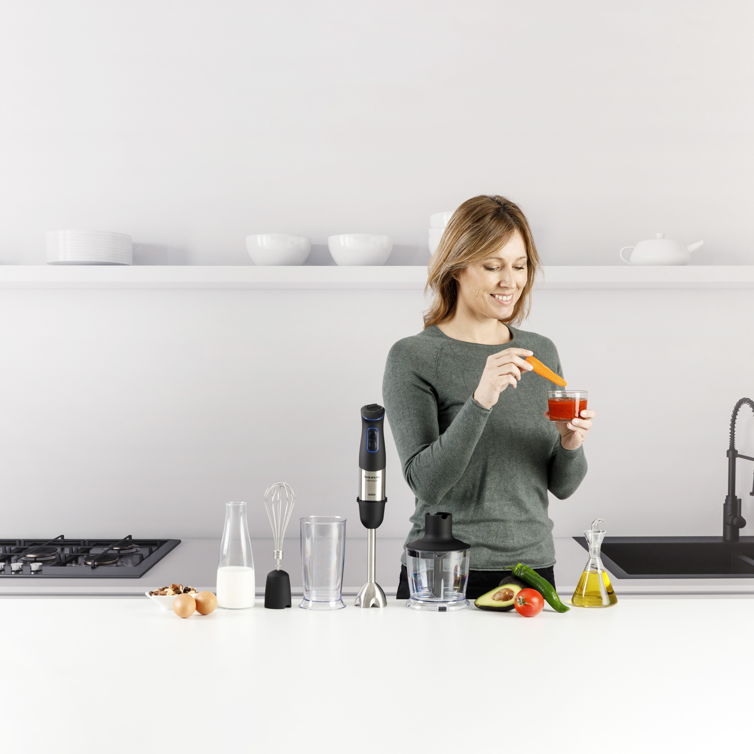 Una mujer añade una zanahoria a una salsa de tomate en un vaso. Electrodomésticos e ingredientes de cocina en la encimera.
