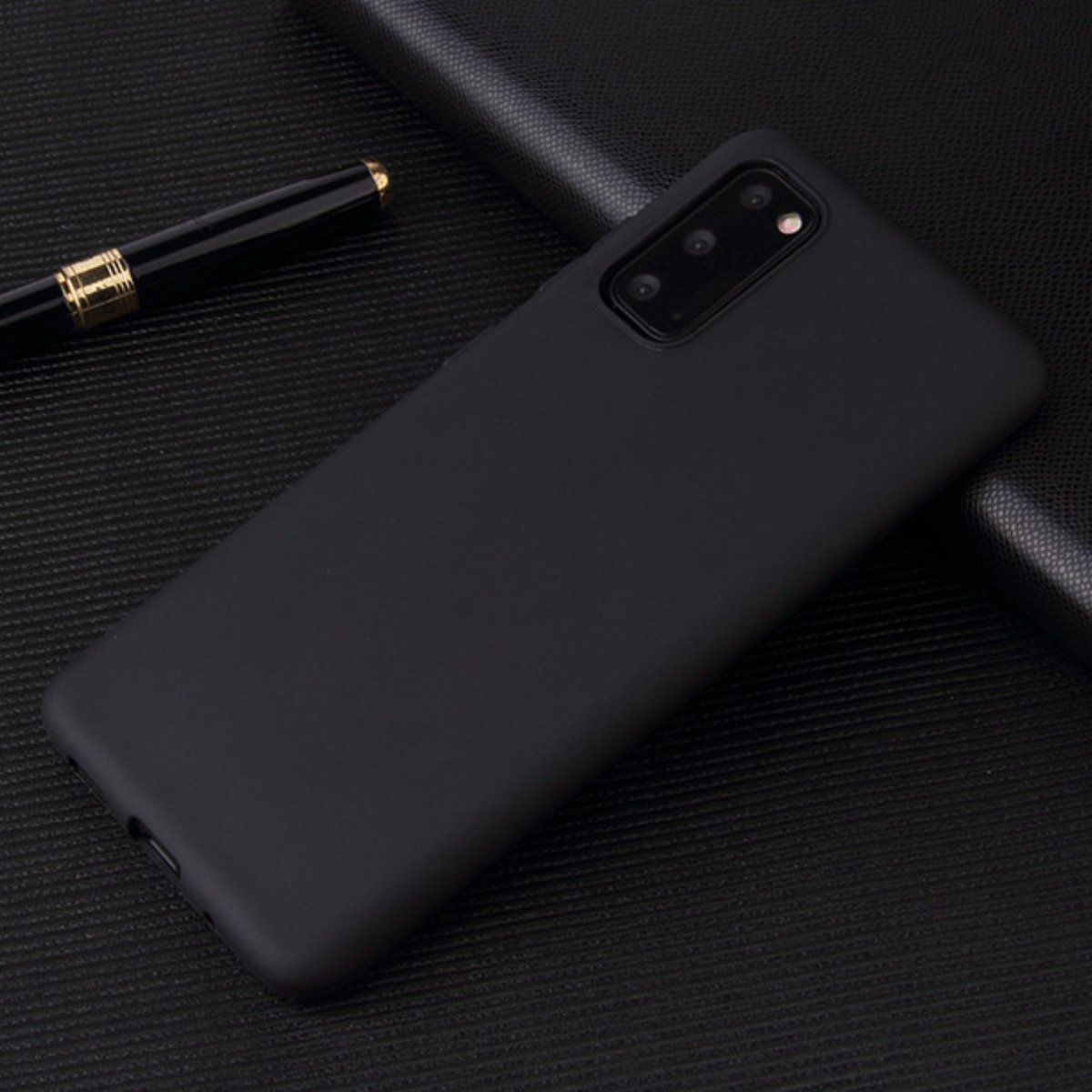 Schwarzes Smartphone mit Dreifachkamera liegt auf einer strukturierten schwarzen Oberfläche neben einem Stift.