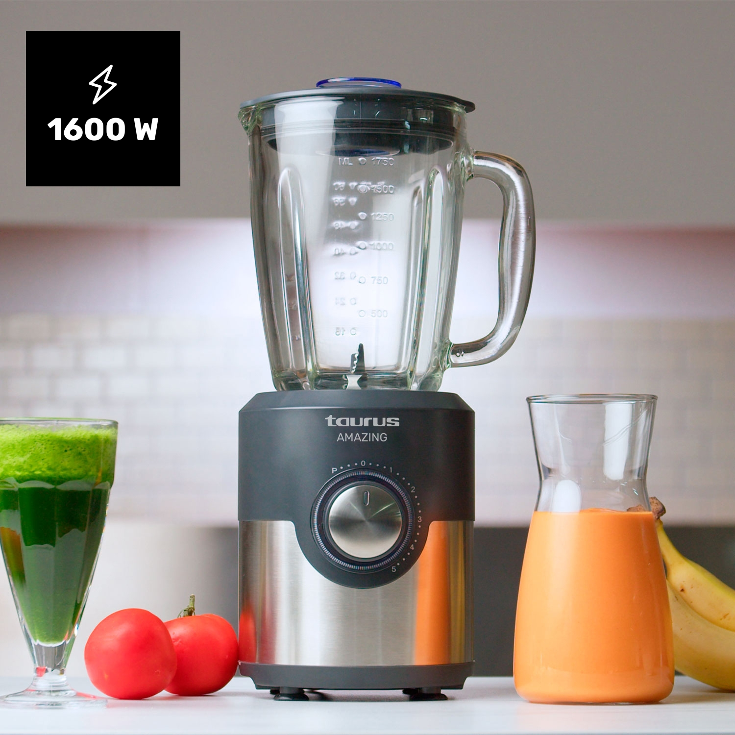 Un frullatore con un boccale di vetro, un bicchiere con succo verde, due pomodori e un bicchiere con succo d'arancia, con banane.