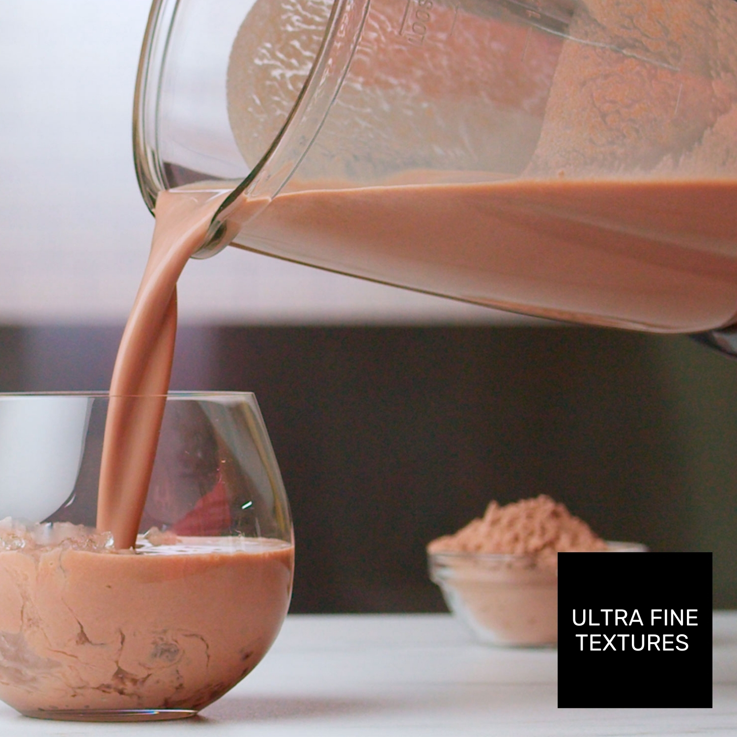 Una bevanda viene versata in un bicchiere con ghiaccio. Una ciotola di cacao in polvere è sullo sfondo. Il testo 'Texture ultra fini' è visibile.