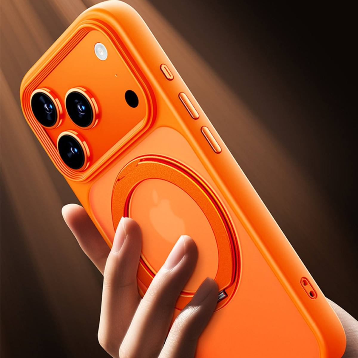 Una custodia arancione per telefono con un anello magnetico circolare è tenuta in mano. Ha tre obiettivi e il logo Apple.