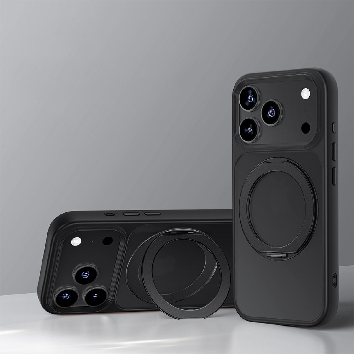Tre custodie nere per telefono con ritagli per fotocamera e supporti ad anello. Una è in posizione verticale, due sono piatte. Tutto su sfondo grigio.