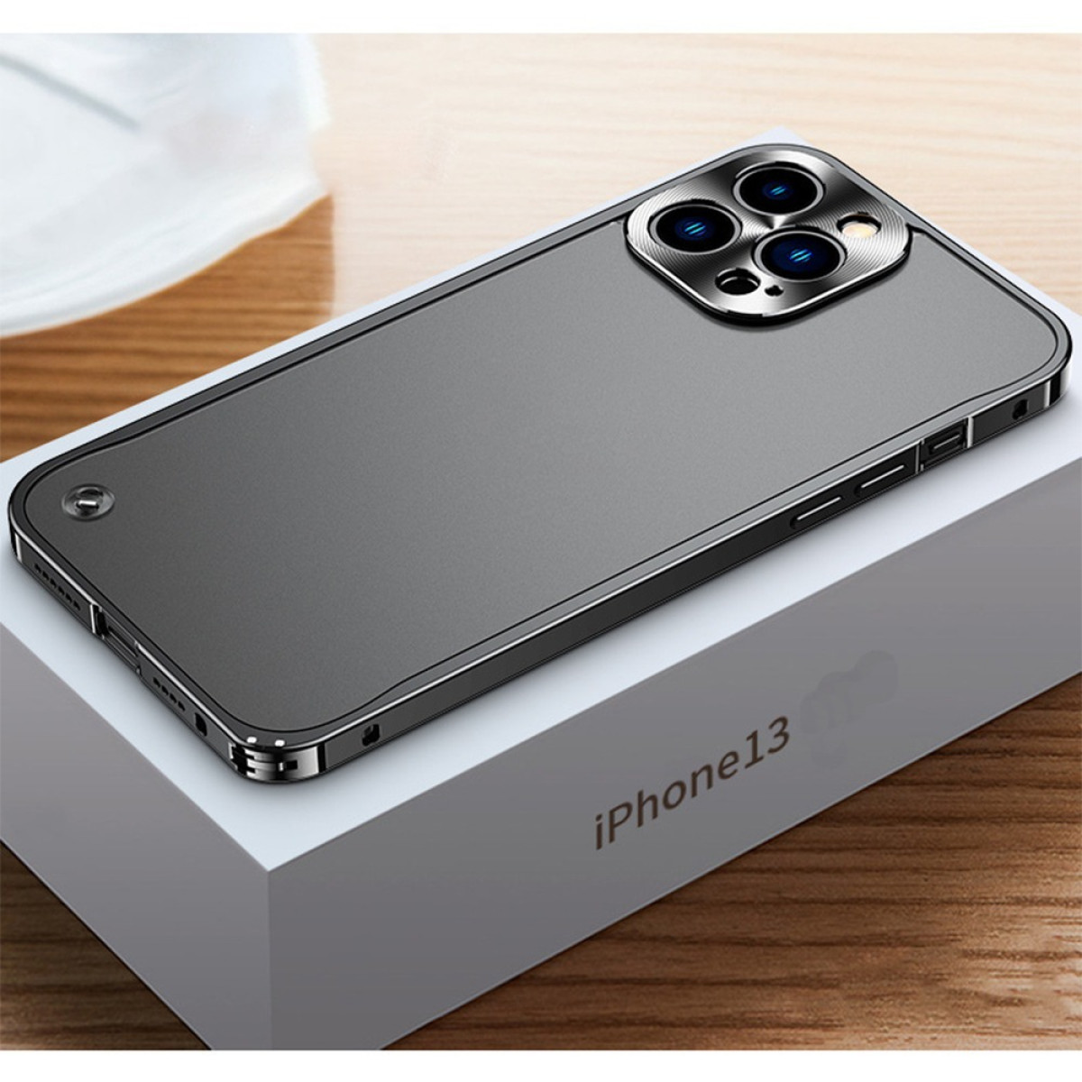 Una custodia grigia per iPhone 13 è appoggiata su una scatola bianca con l'etichetta iPhone13. La custodia ha un rigonfiamento della fotocamera e una cornice argentata.