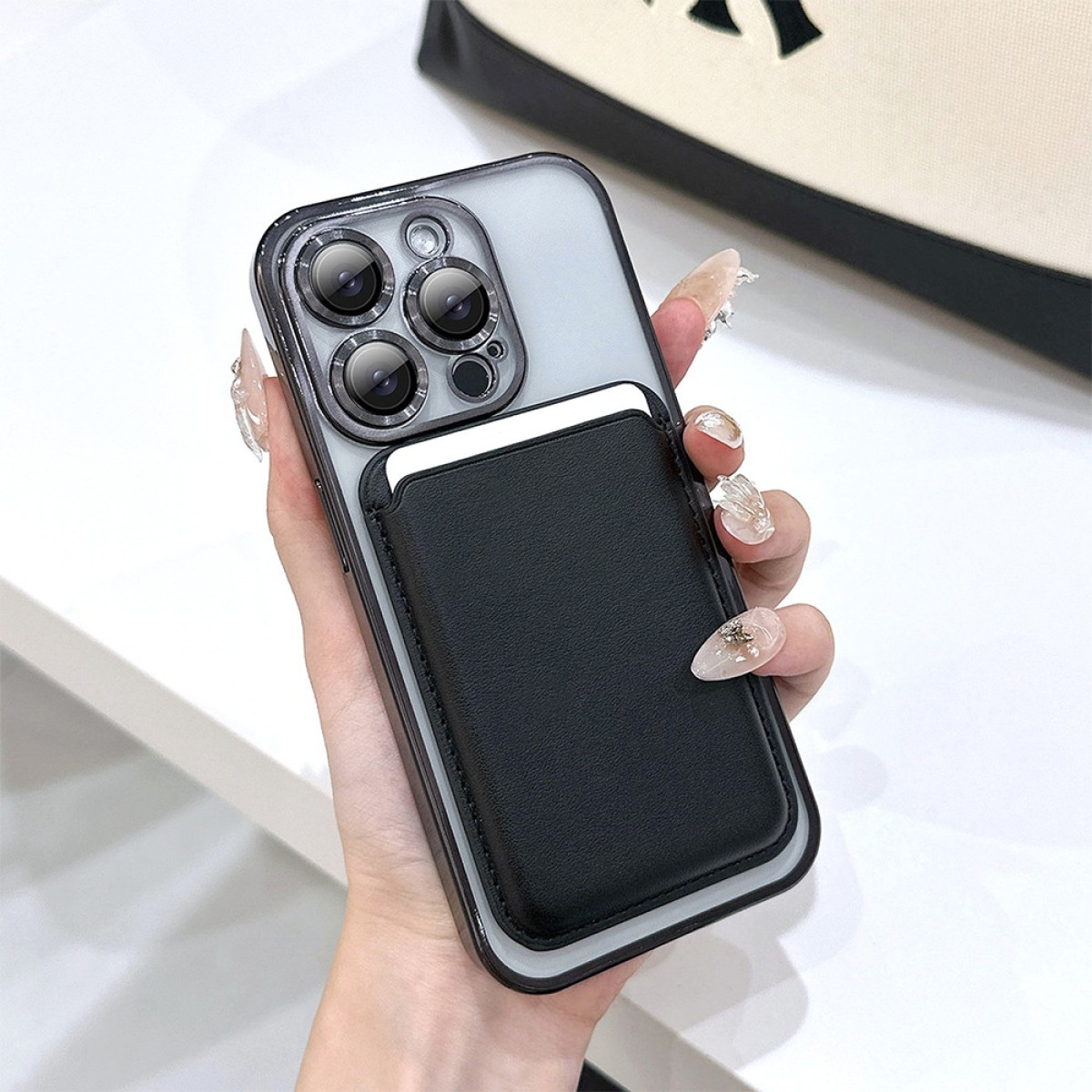 Una mano tiene una custodia per telefono con un portafoglio nero attaccato. Il telefono ha tre obiettivi. Le unghie sono dipinte.