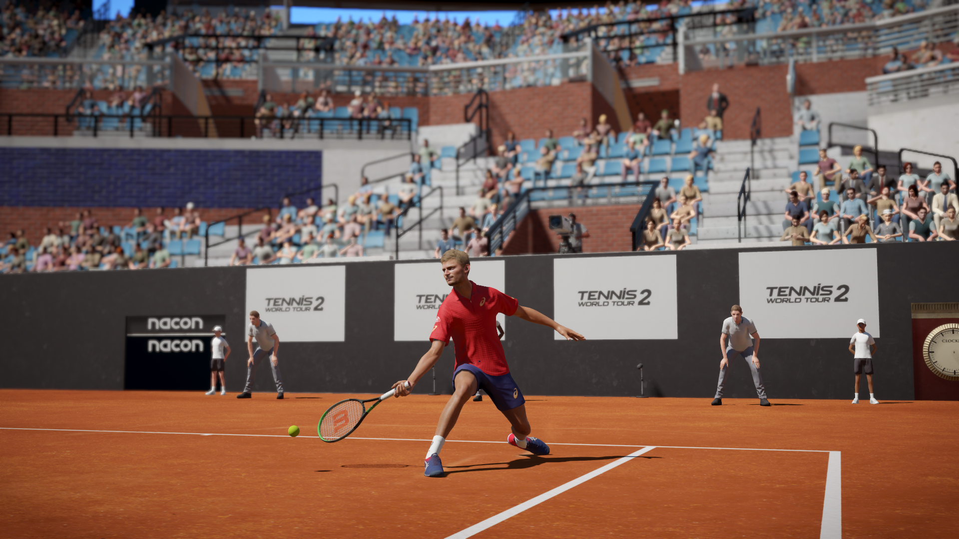 Ein Tennisspieler im roten Hemd schlägt einen Ball auf einem Sandplatz. Zuschauer füllen die Tribüne. Logos sind sichtbar.