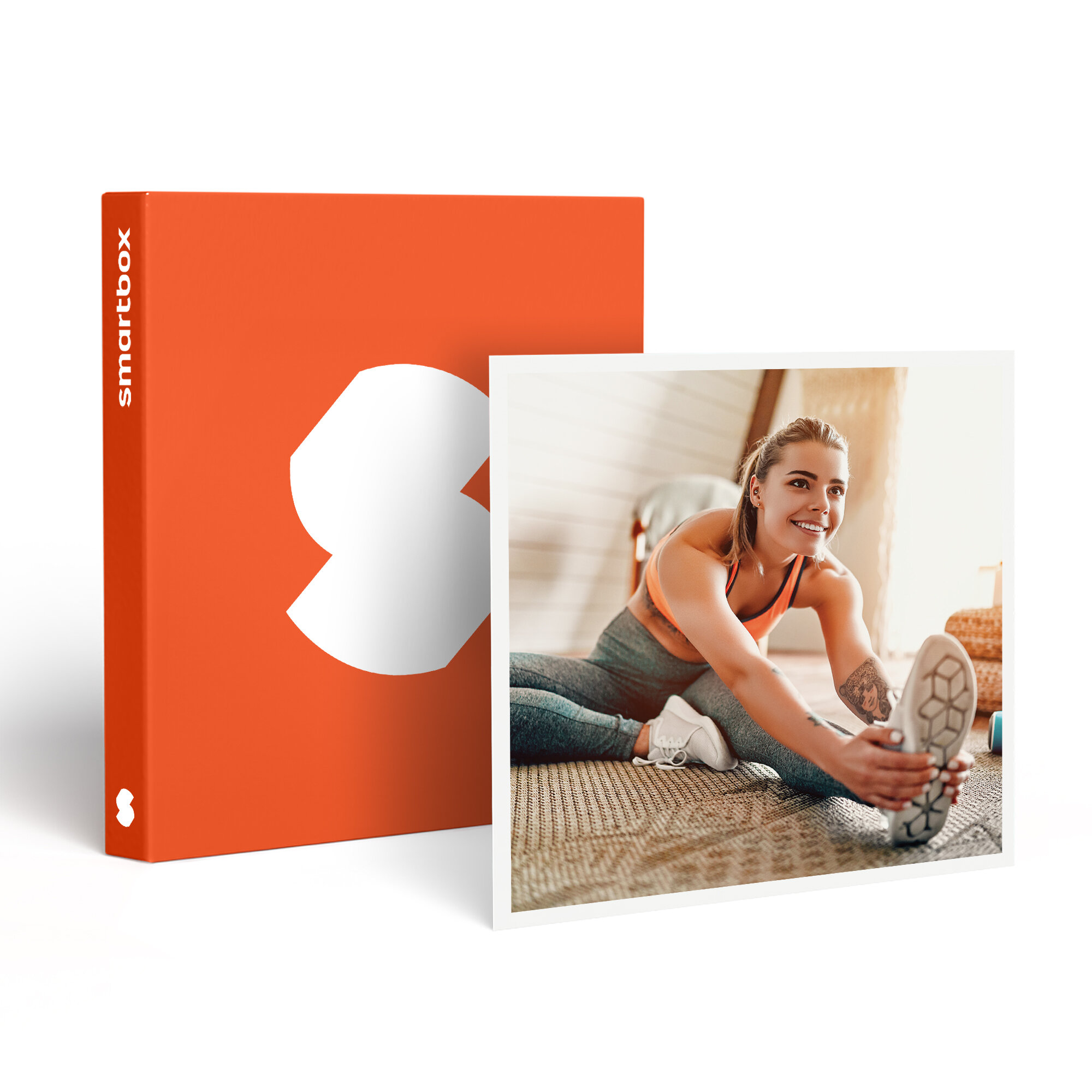 Mujer estira la pierna, sonriendo, cerca de Smartbox naranja. Lleva ropa deportiva. Fondo: habitación, alfombra y luz solar.