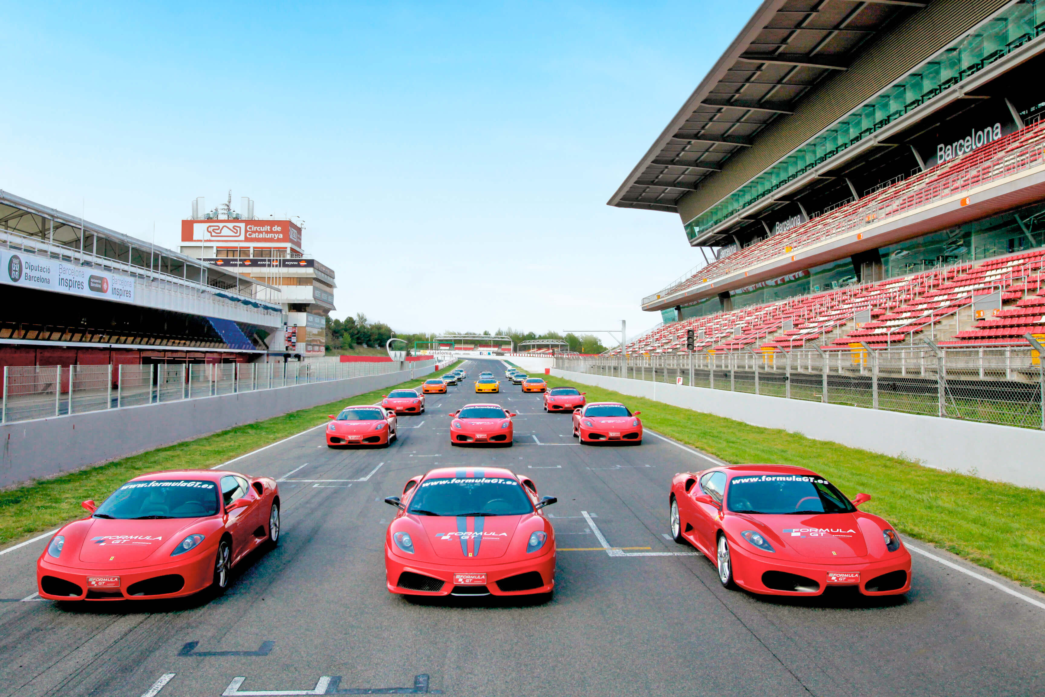 Coches rojos Formula GT alineados en un circuito. Detrás, gradas y cielo azul.