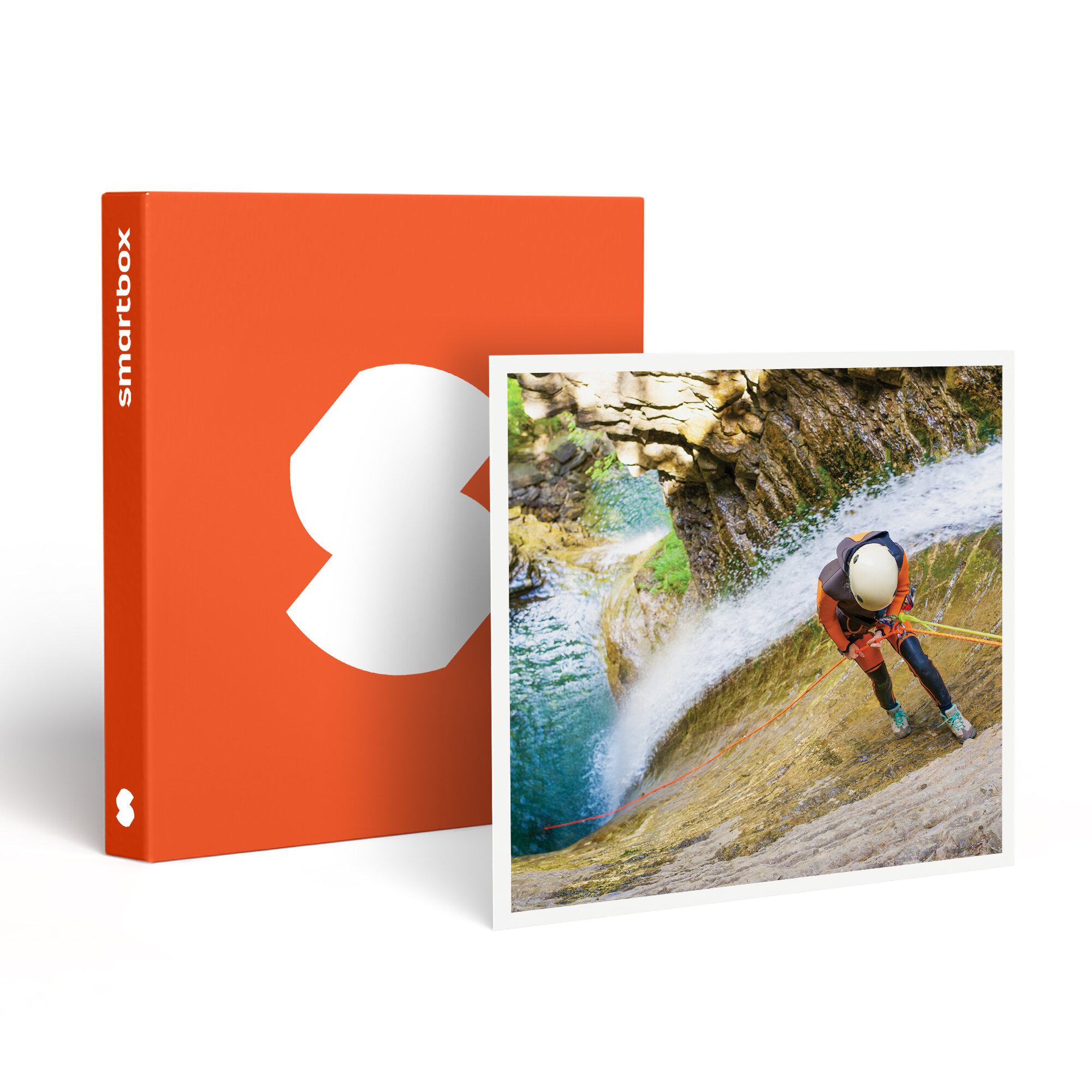 Una persona desciende en rápel por una cascada. Lleva casco y equipo de seguridad. Una caja naranja con un logotipo blanco está cerca.