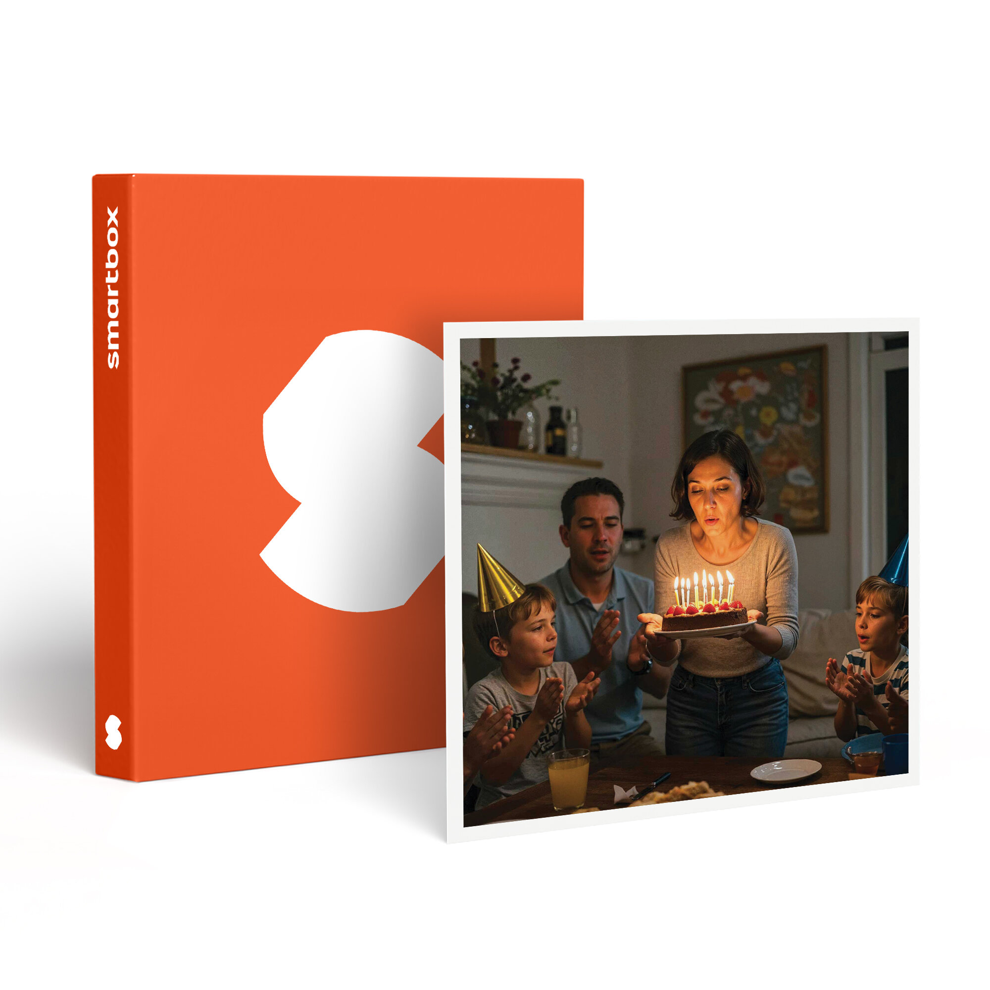 Una familia celebra un cumpleaños. Una mujer sopla las velas de un pastel. Hay niños y adultos. Hay una caja naranja en el fondo.